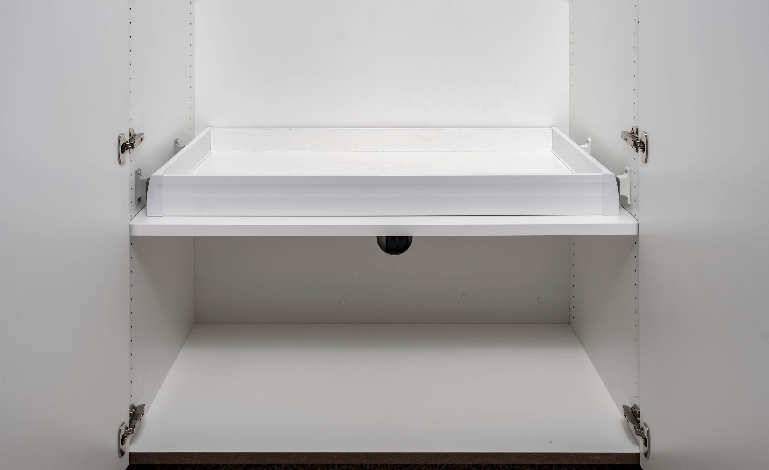 Empty white kitchen cabinet with a pull-out shelf and a hidden camera below the shelf.