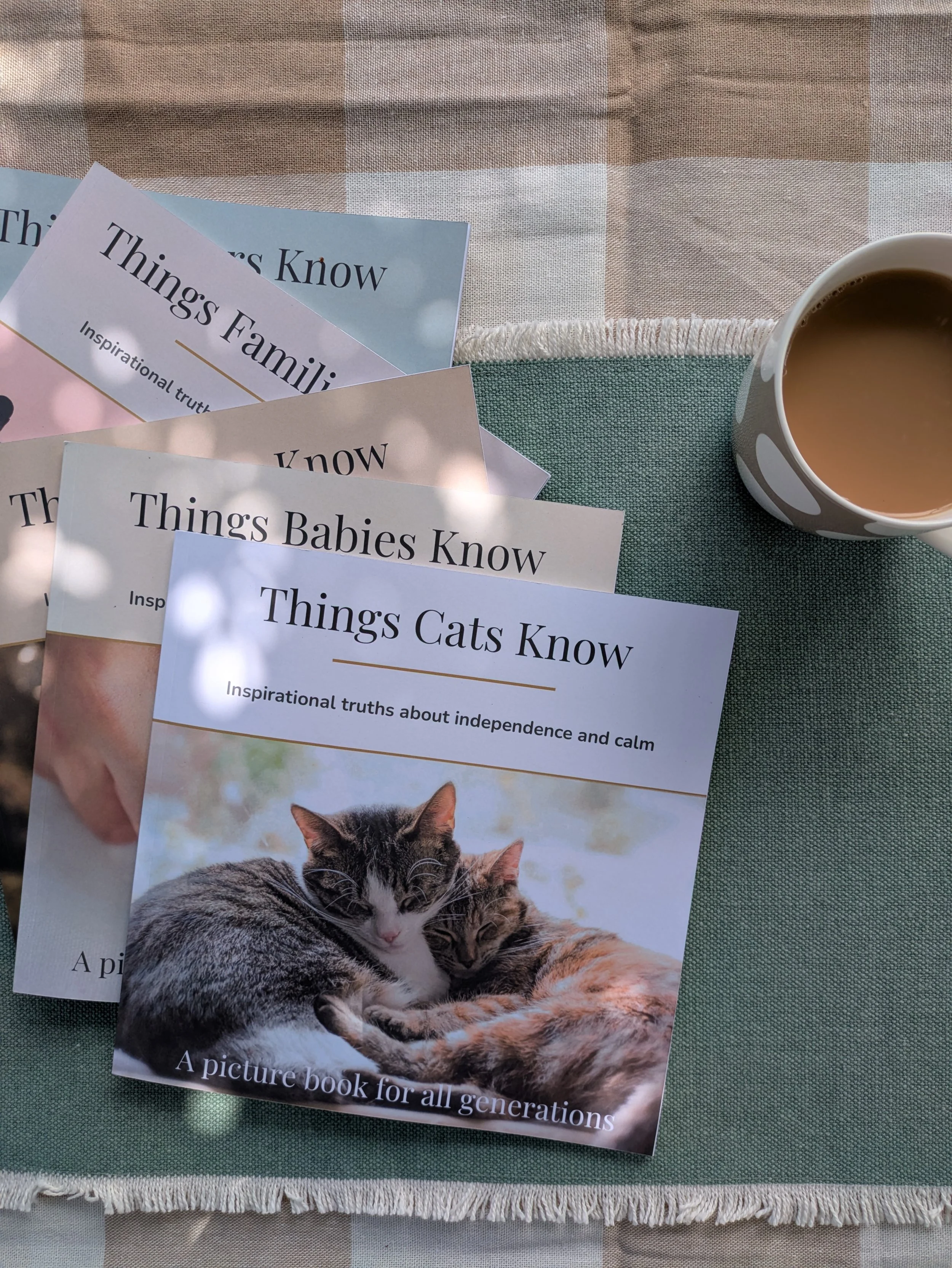 A collection of pamphlets titled 'Things Babies Know,' 'Things Cats Know,' and 'Things Families Know' on a green tablecloth with a cup of coffee nearby.
