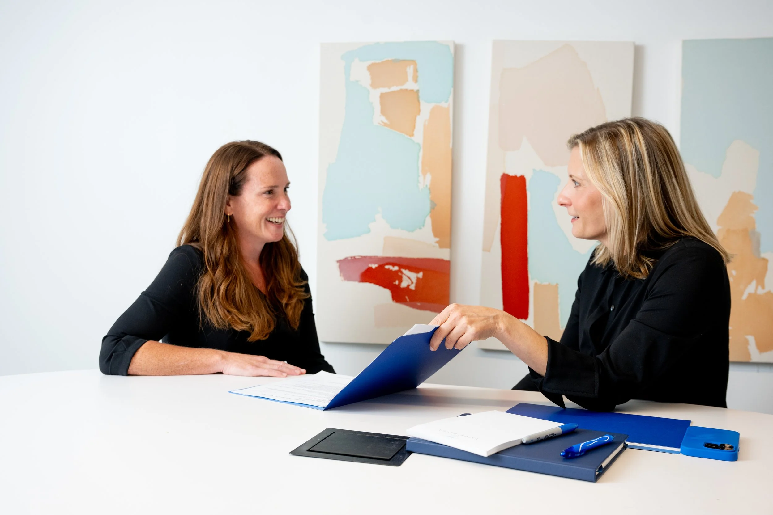 Paige Panda handing a document to a smiling colleague across a table