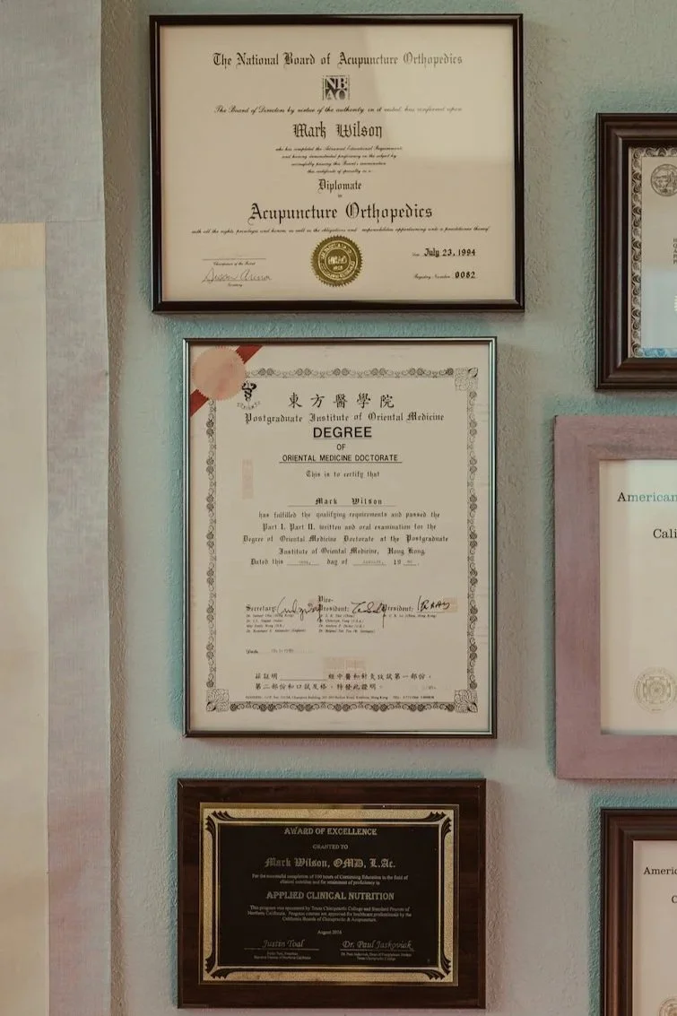 Framed medical and acupuncture certifications displayed on the office wall, showing Dr. Mark Wilson’s advanced training and decades of experience in Traditional Chinese Medicine.