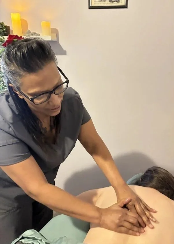 A woman getting a back massage from a therapist in a room with candles and wall decor.