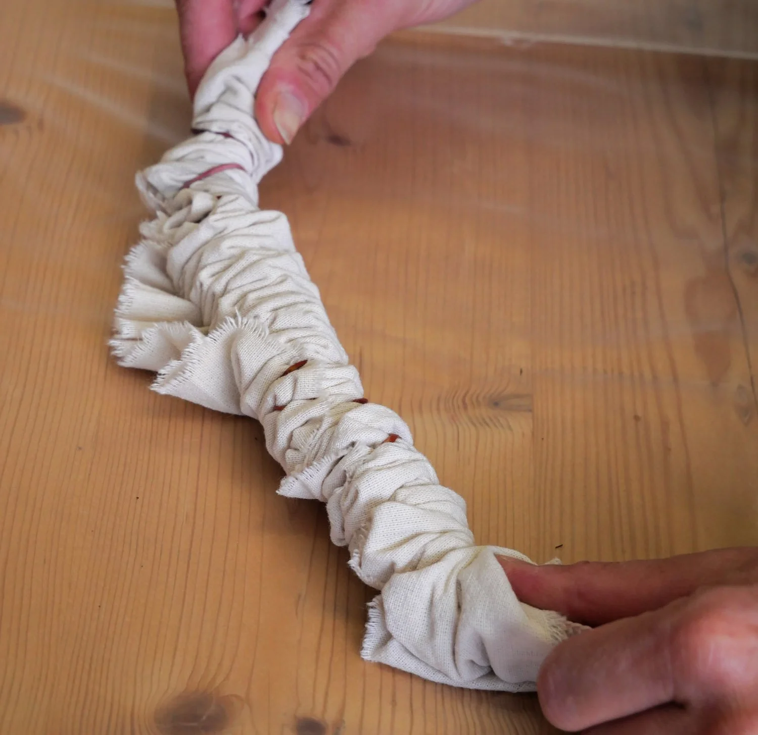 Une personne manipule une corde en tissu blanc tressée ou enroulée, posée sur une surface en bois.