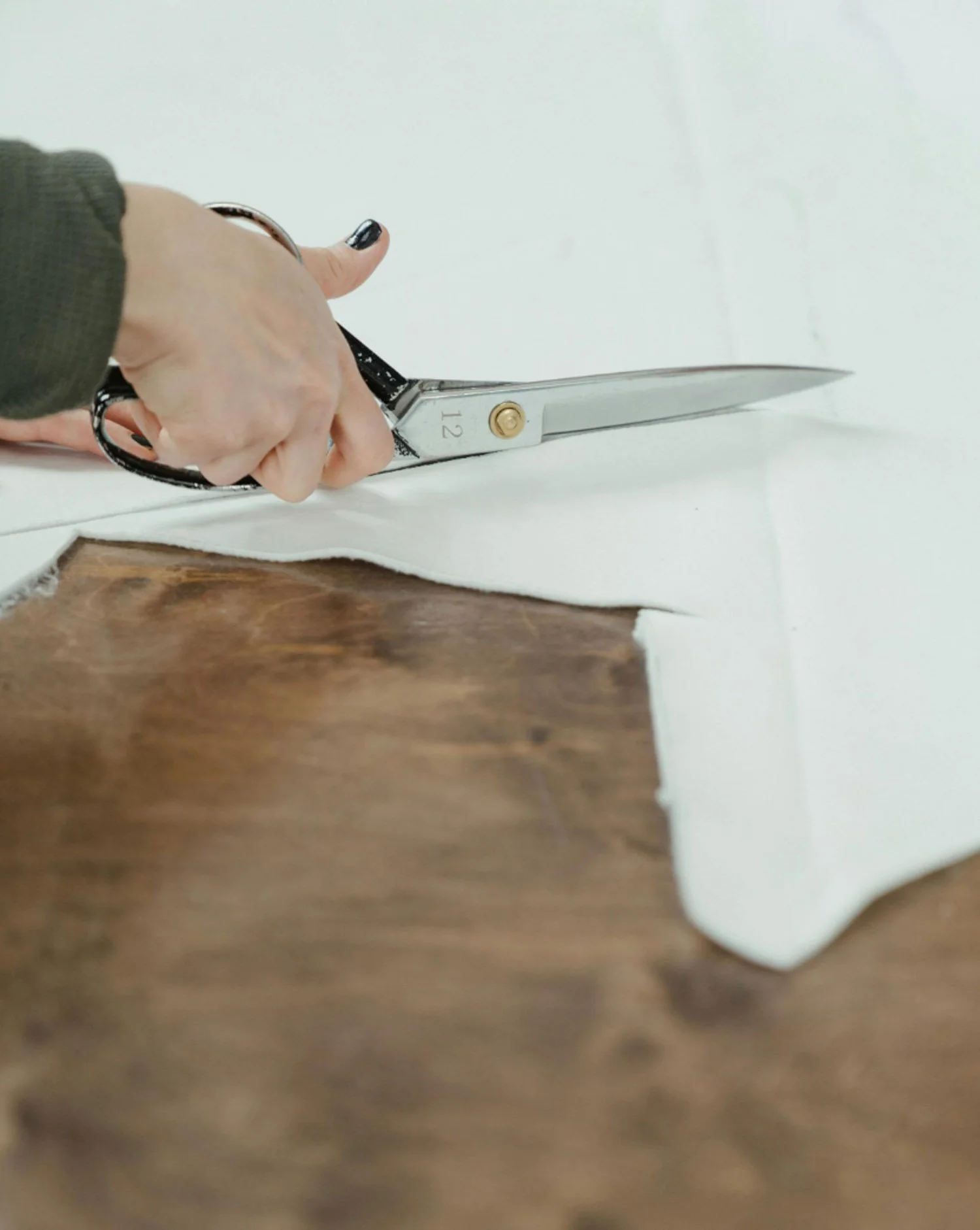 Une personne utilisant des ciseaux pour couper un tissu blanc sur une surface en bois.