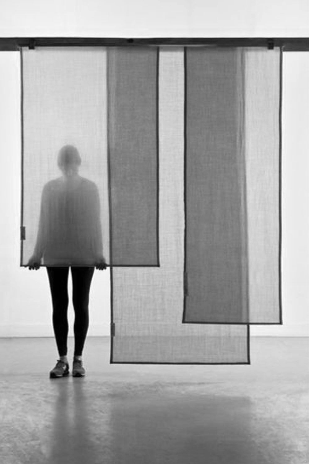 Une silhouette de femme debout derrière des panneaux translucides dans une pièce noire et blanche.