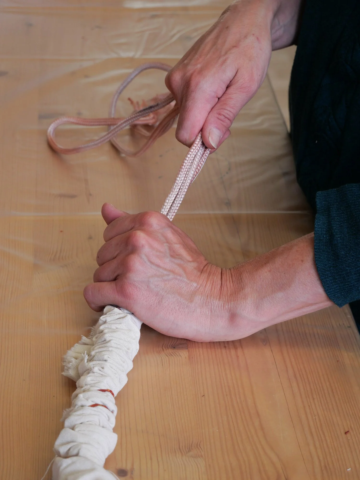 Main d'une personne tenant une corde d'escalade ou de sport, avec un nœud, sur une surface en bois.