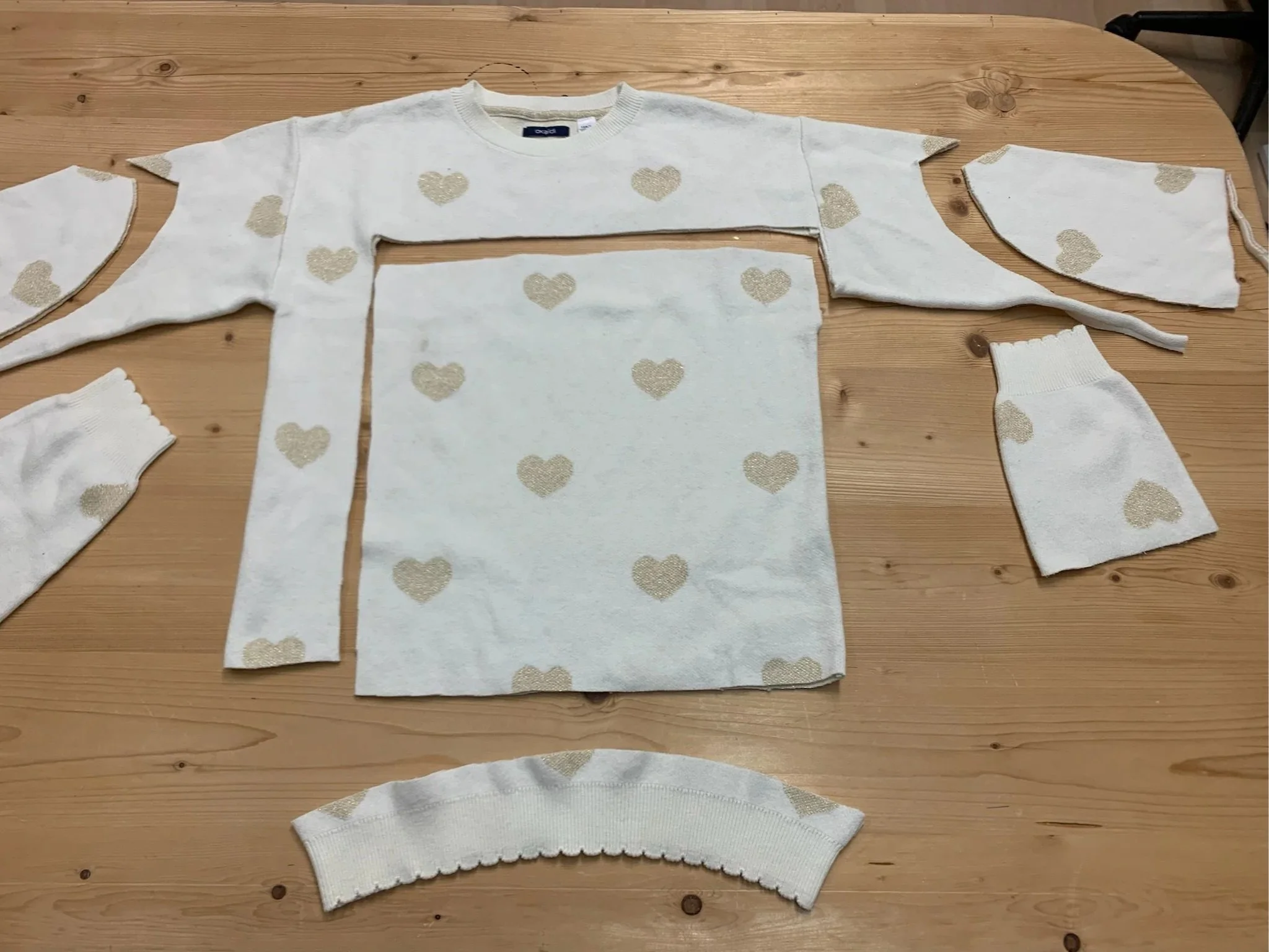 Une serviette de bain blanche avec des cœurs dorés, déployée pour révéler différentes parties d'une tenue de bain, avec d'autres pièces coordonnées autour.