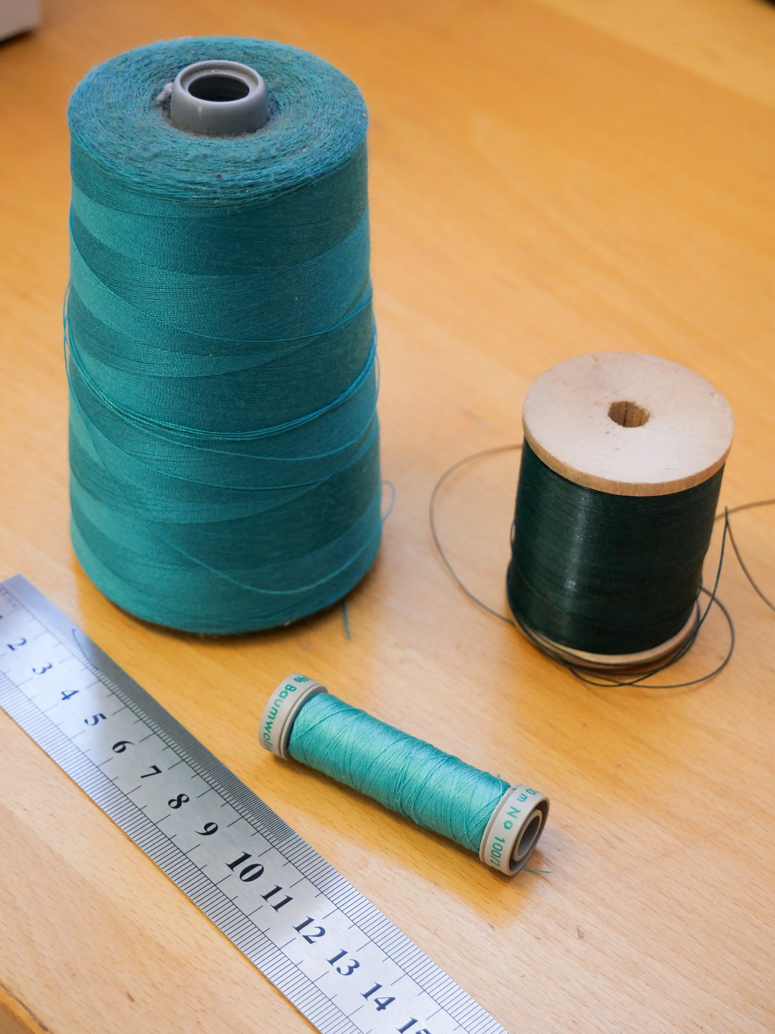 Bobines de fil de couture en différents couleurs et une règle en métal sur une surface en bois.