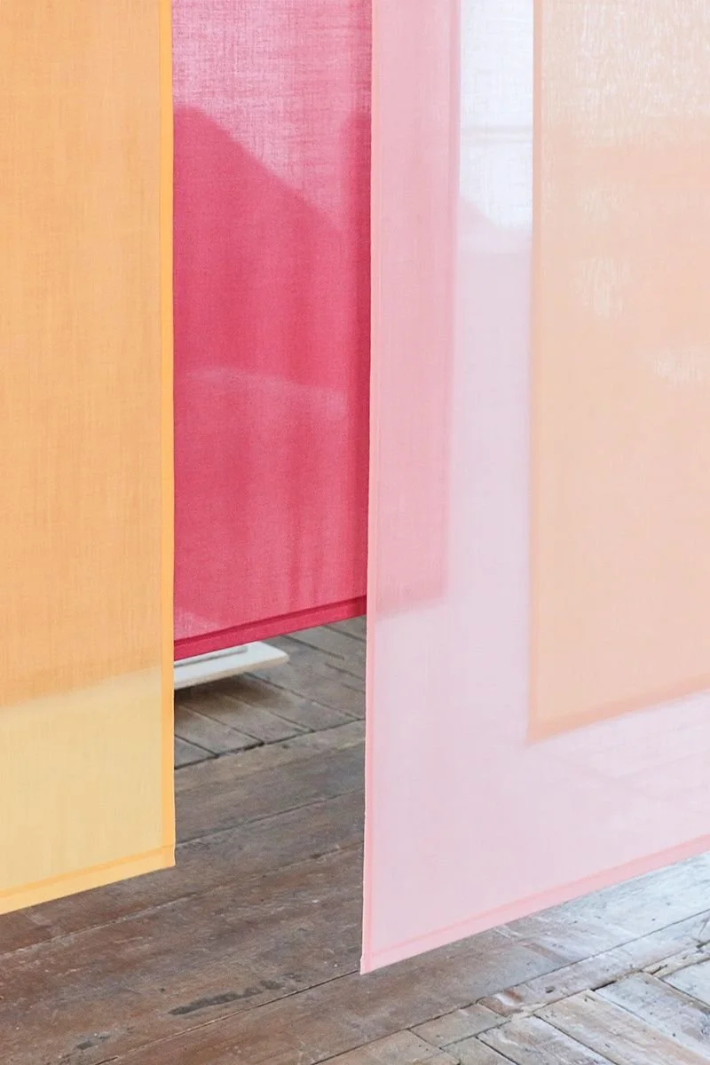 Portes en tissu de différentes couleurs pastel, notamment jaune, rose et beige, partiellement ouvertes dans une pièce au sol en bois.