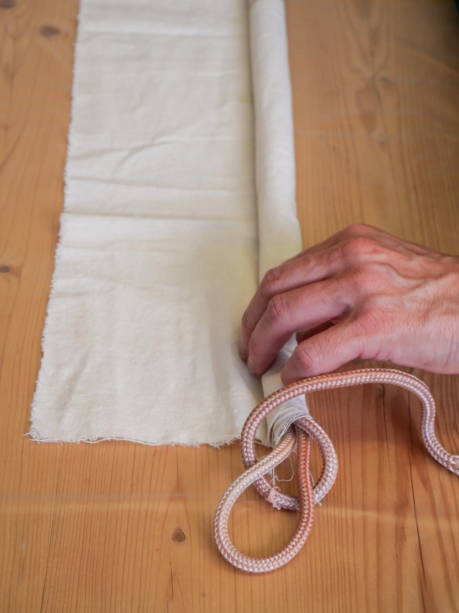 Main tenant une corde enroulée à côté d'un morceau de tissu sur une table en bois.