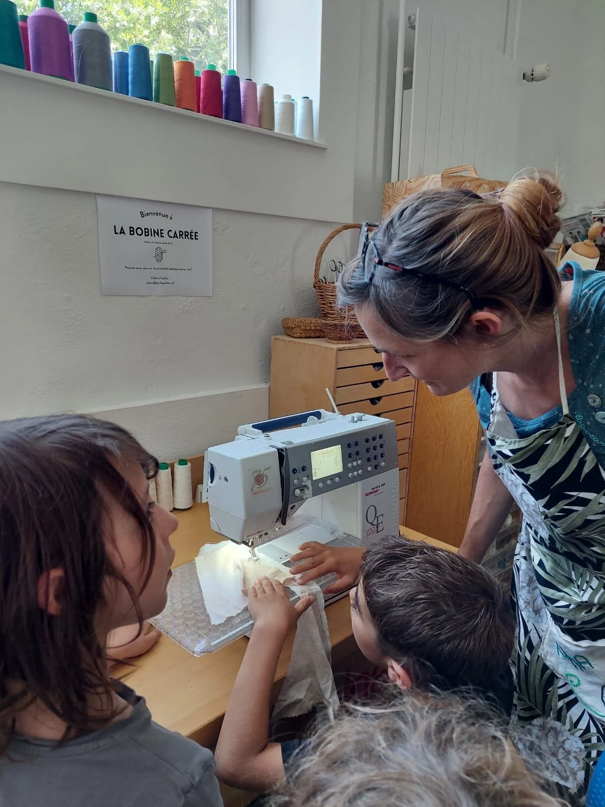 Une femme montre à des enfants comment utiliser une machine à coudre dans un atelier de couture.