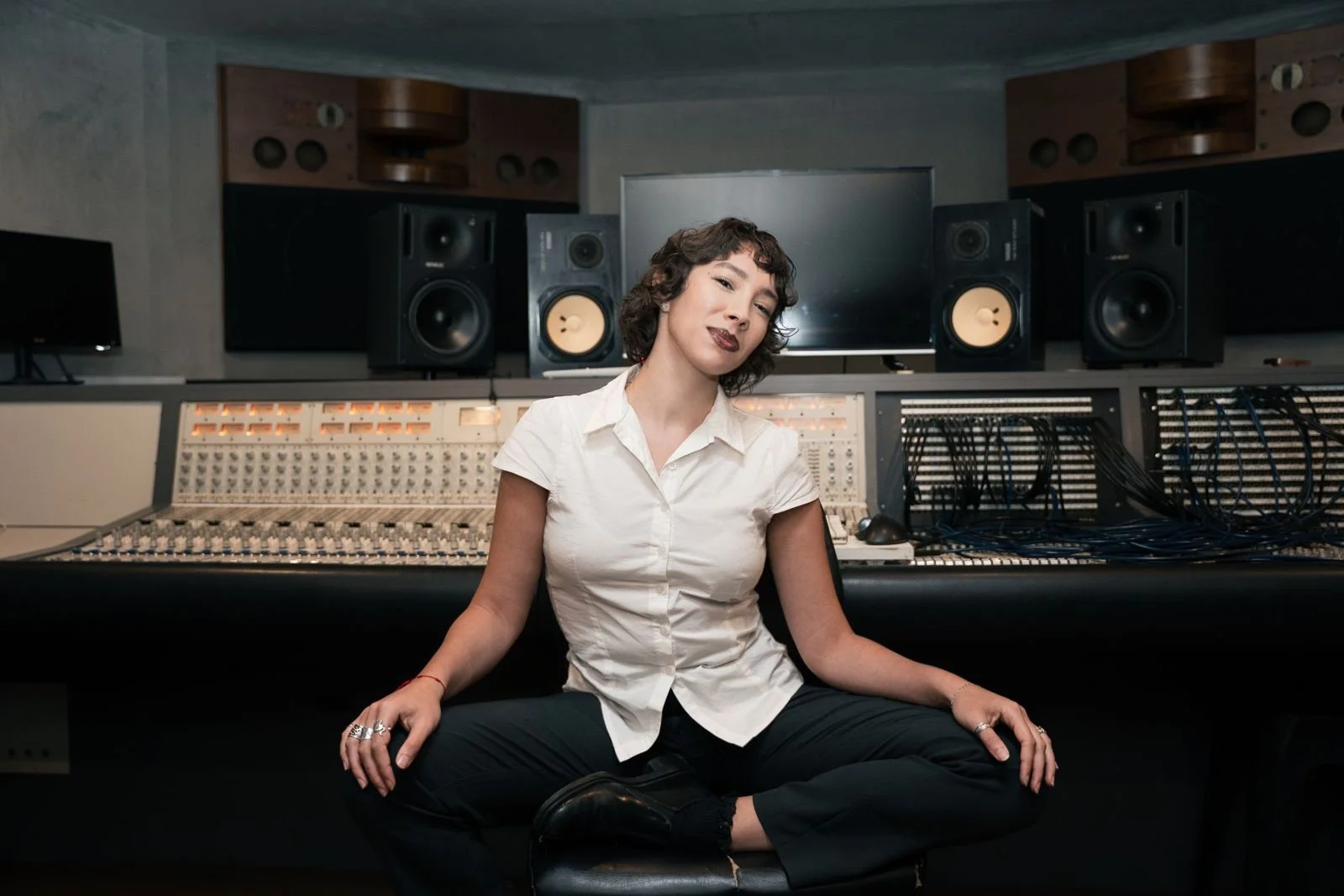 Mujer sentada en un estudio de grabación con mezcla de audio y altavoces detrás.