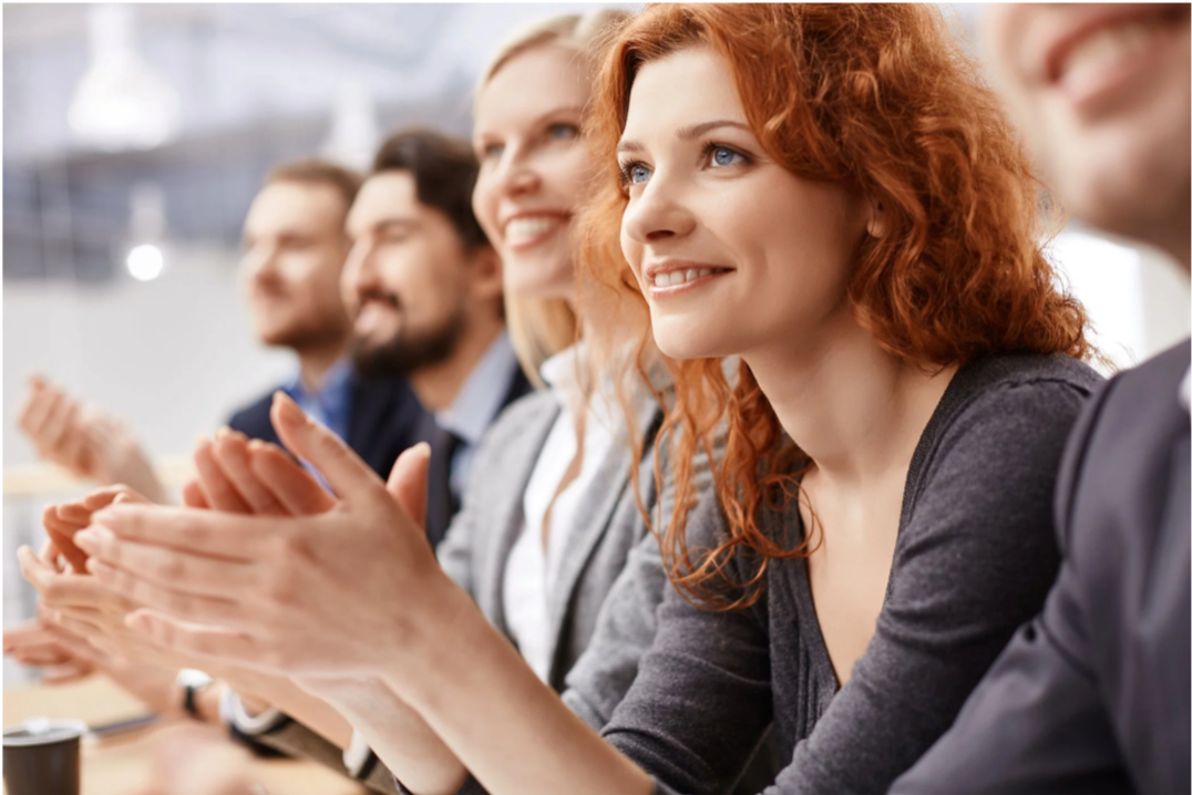A group of diverse people clapping and smiling at a meeting or event.