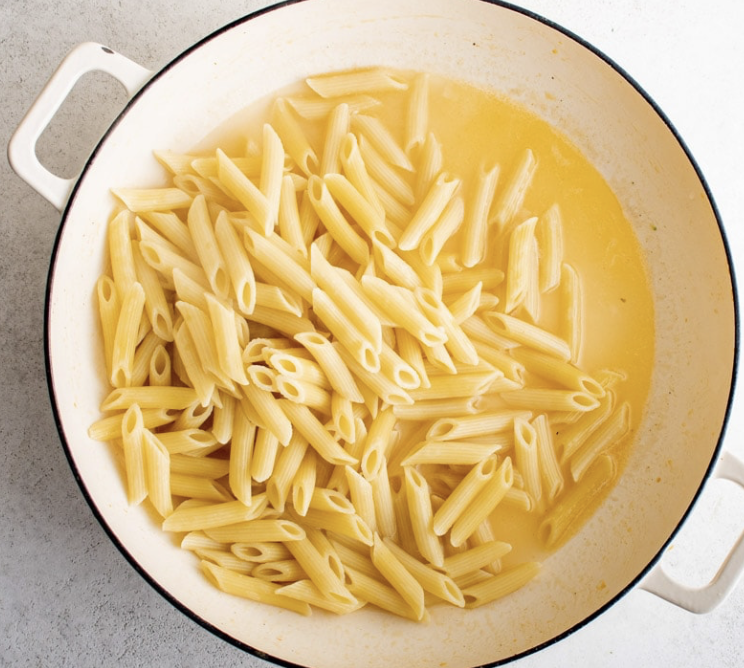 A white plate of cooked penne pasta with meat sauce and black pepper, served on a wooden surface.