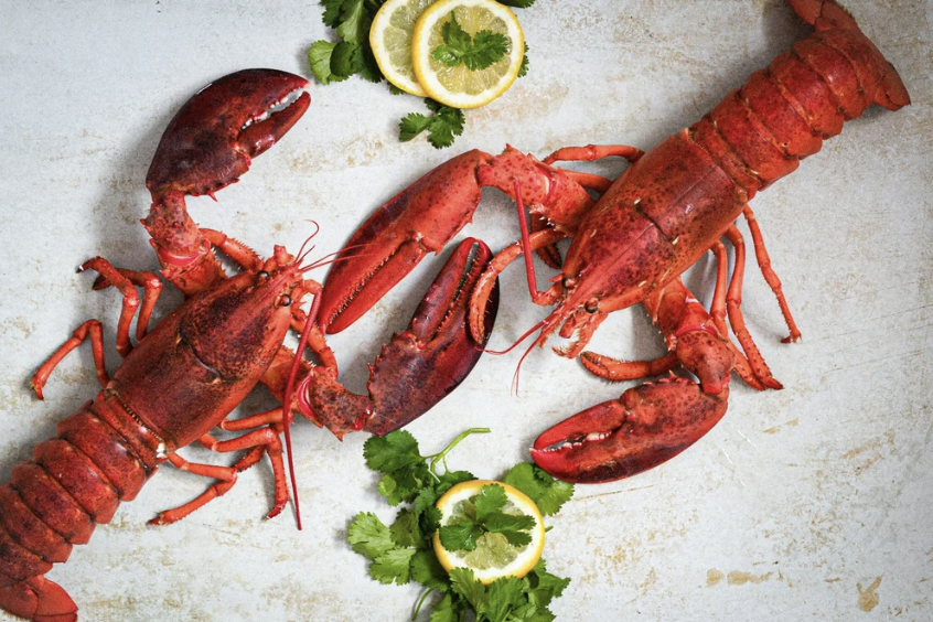 Two cooked lobsters, lemon slices, and cilantro on a light surface.