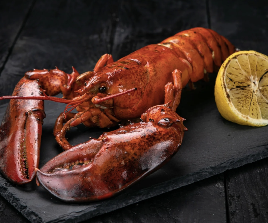 Cooked lobster with lemon slices and cilantro on a light-colored surface.