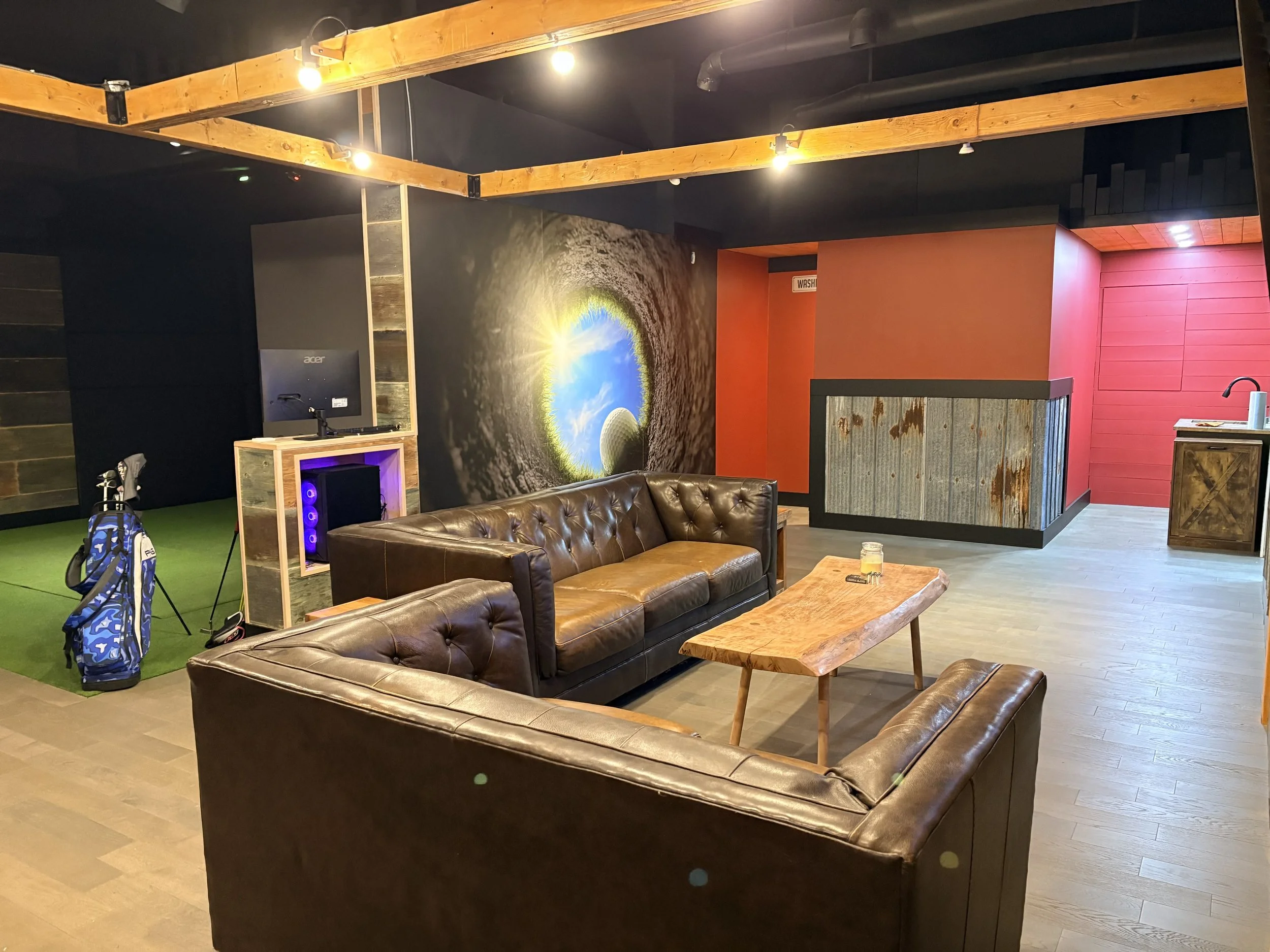 Interior of a lounge with leather couches, wooden coffee table, a small kitchen area, and a large wall mural of the earth seen from underground