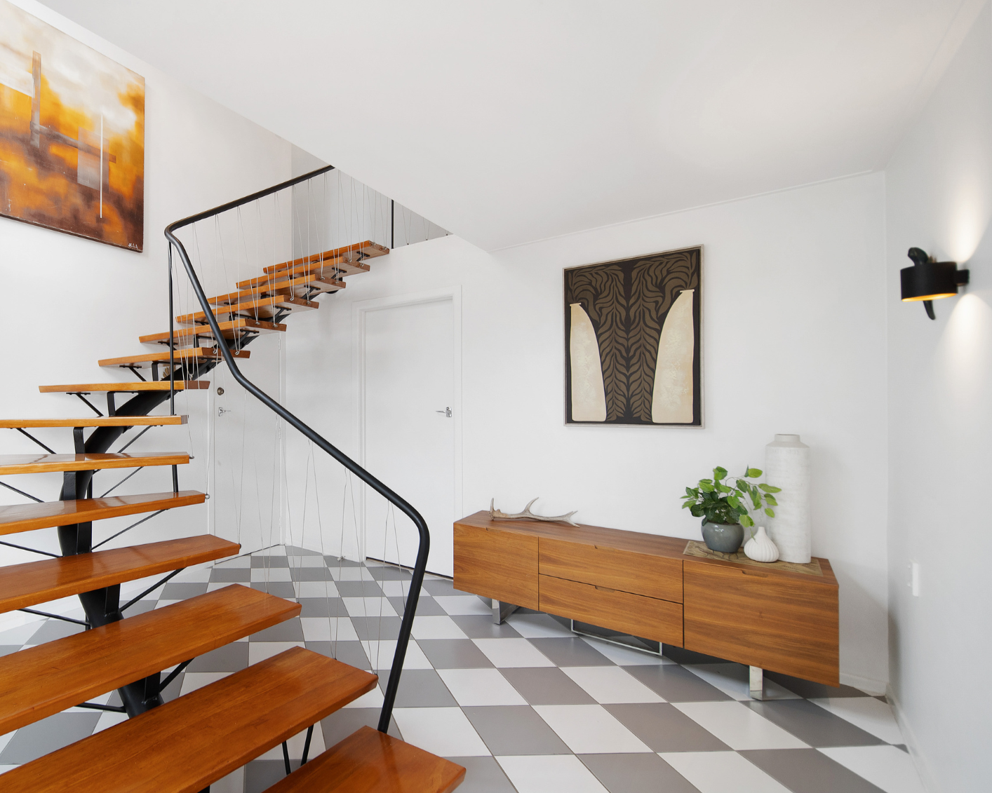 Modern interior with a staircase, wooden sideboard, artwork, plants, and decorative items.