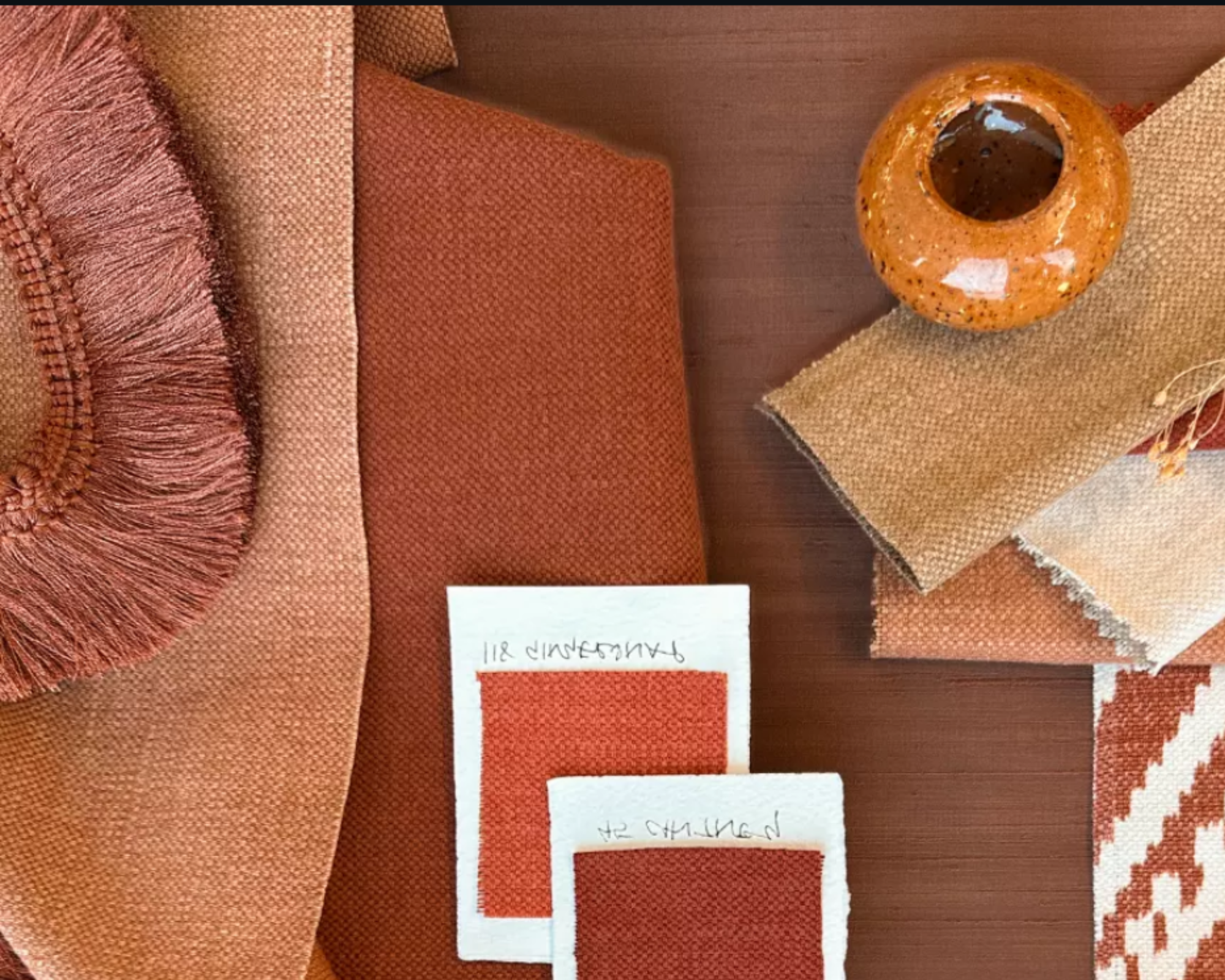 Color swatches, fabric samples, and a terracotta vase on a wooden surface.
