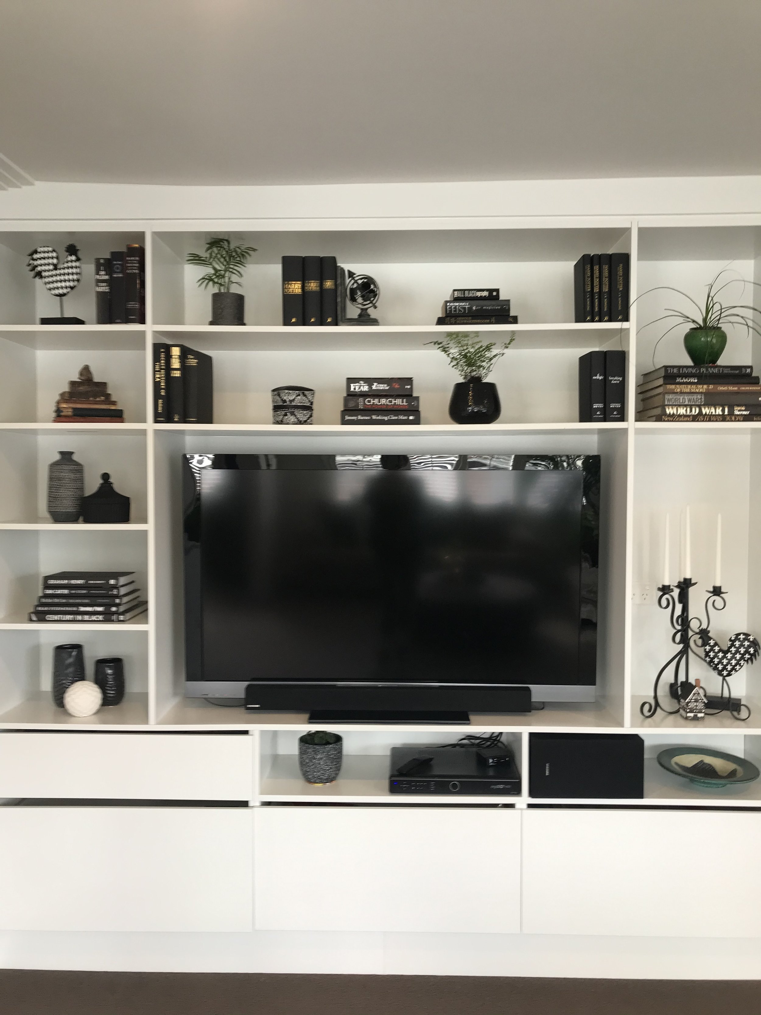 A white entertainment center with black and green decorative objects, books, and a large flat-screen TV in the center.