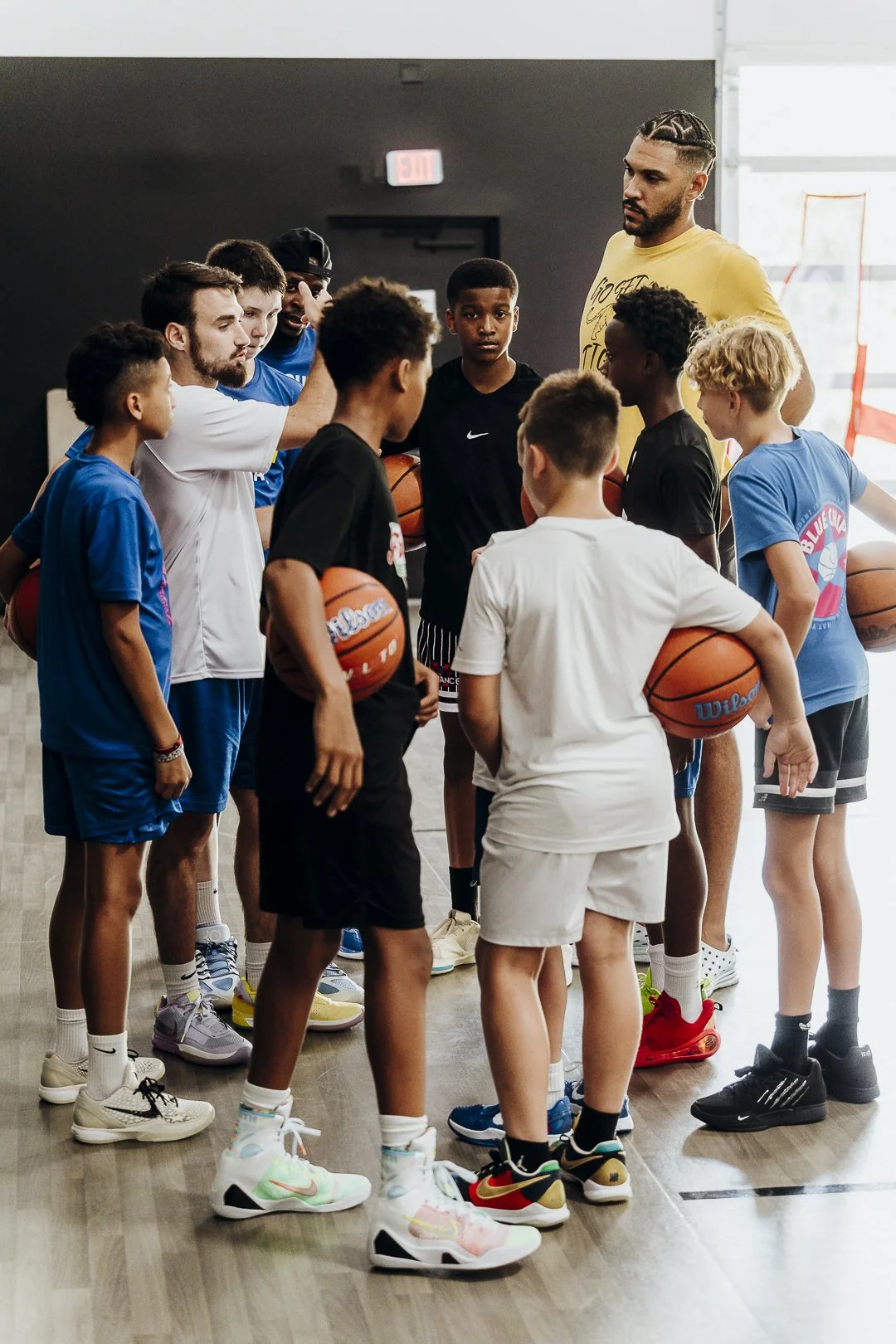 Group of young basketball players and their coach listening attentively during a timeout or team meeting in a gym.