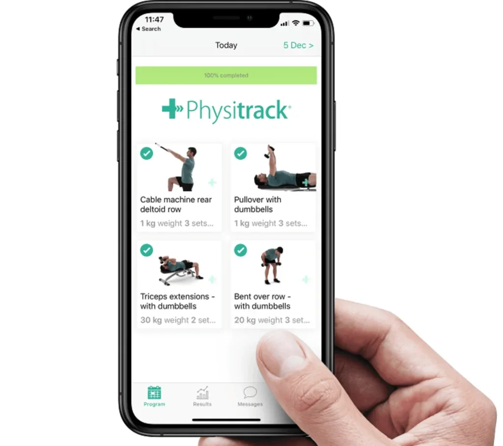 A person holding a smartphone displaying the Physitrack app with a workout program, showing four exercises related to weight training with dumbbells.