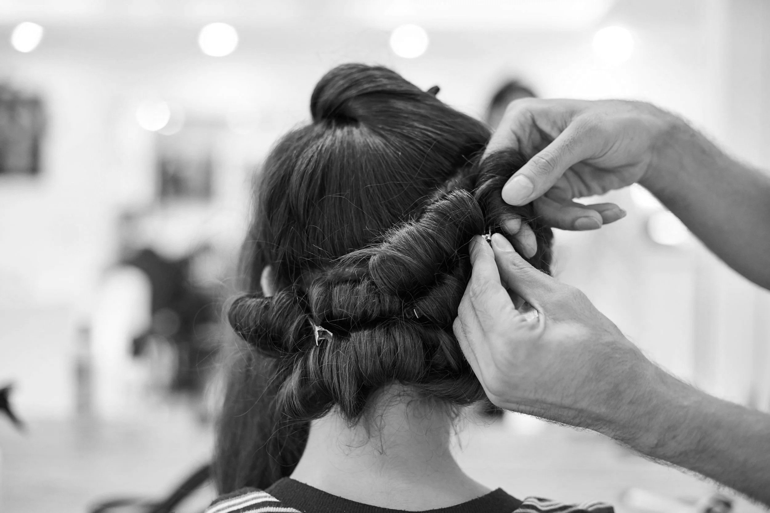 A hairstylist braiding a person's hair in a salon, black and white photo.