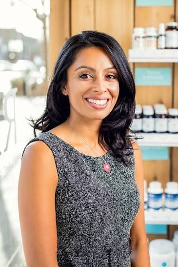 Woman smiling in a store with shelves of bottles behind her.