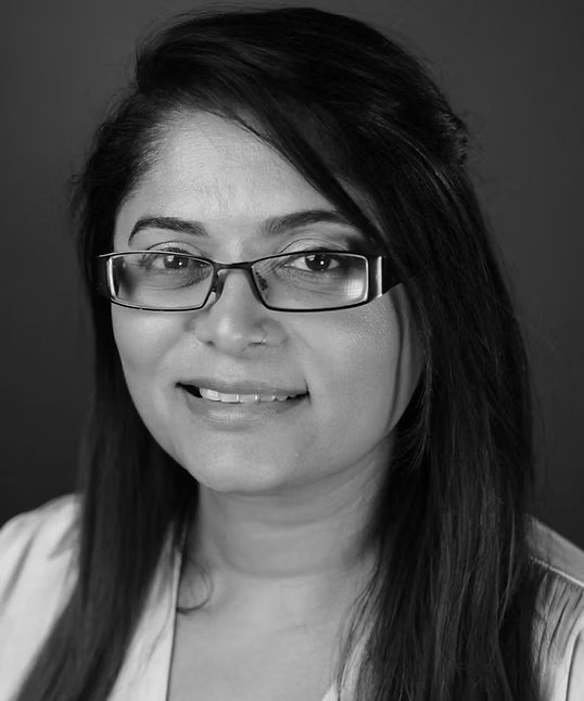 Black and white portrait of a woman with glasses and long dark hair, smiling slightly.