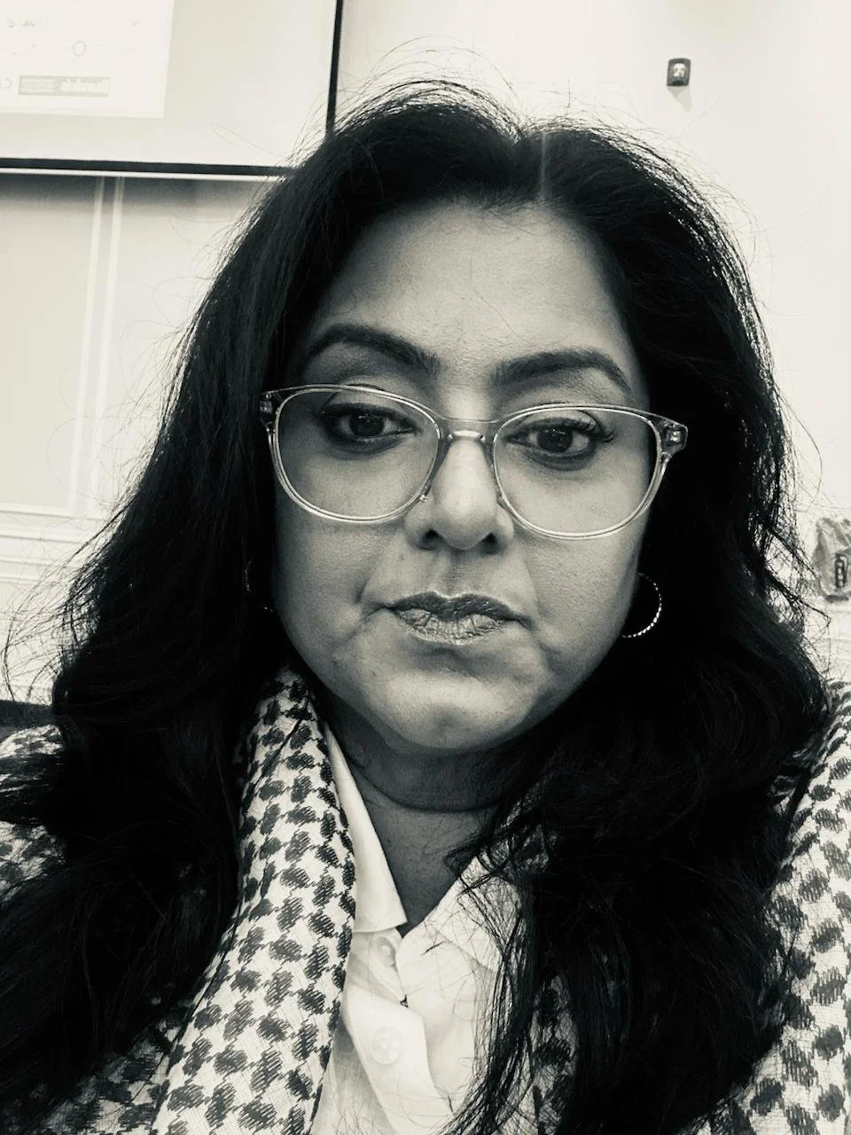 Black and white close-up photo of a woman with long dark hair, wearing glasses, a white blouse, and a patterned scarf.