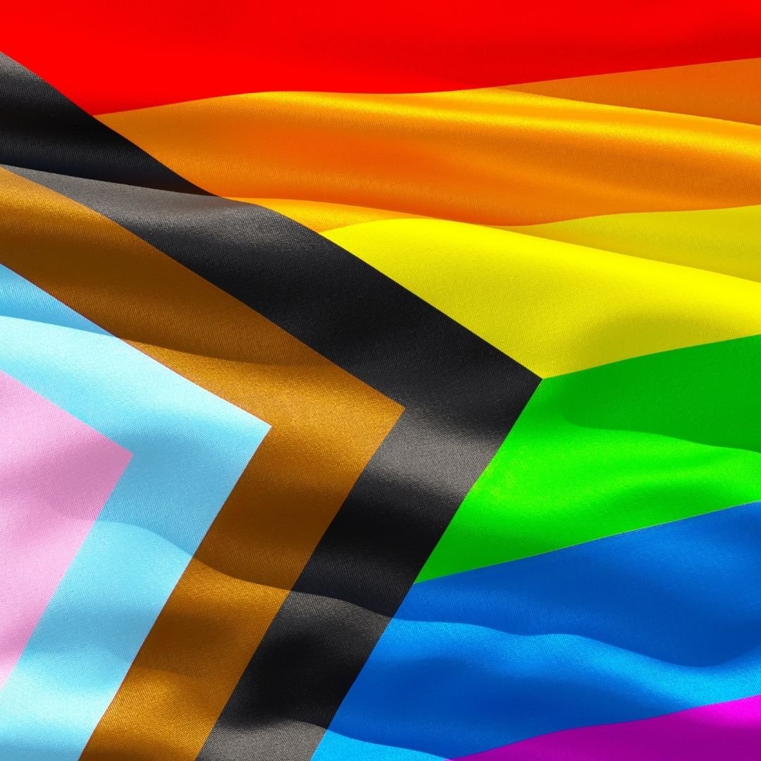 Close-up of the progressive rainbow pride flag, showing red, orange, yellow, green, blue, and pink stripes.