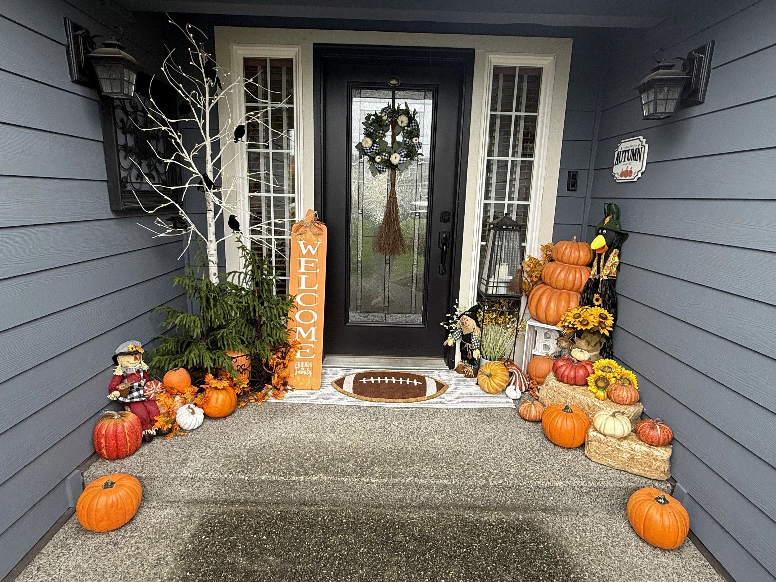 Front porch decorated for autumn with pumpkins, sunflowers, scarecrows, and fall-themed decorations.