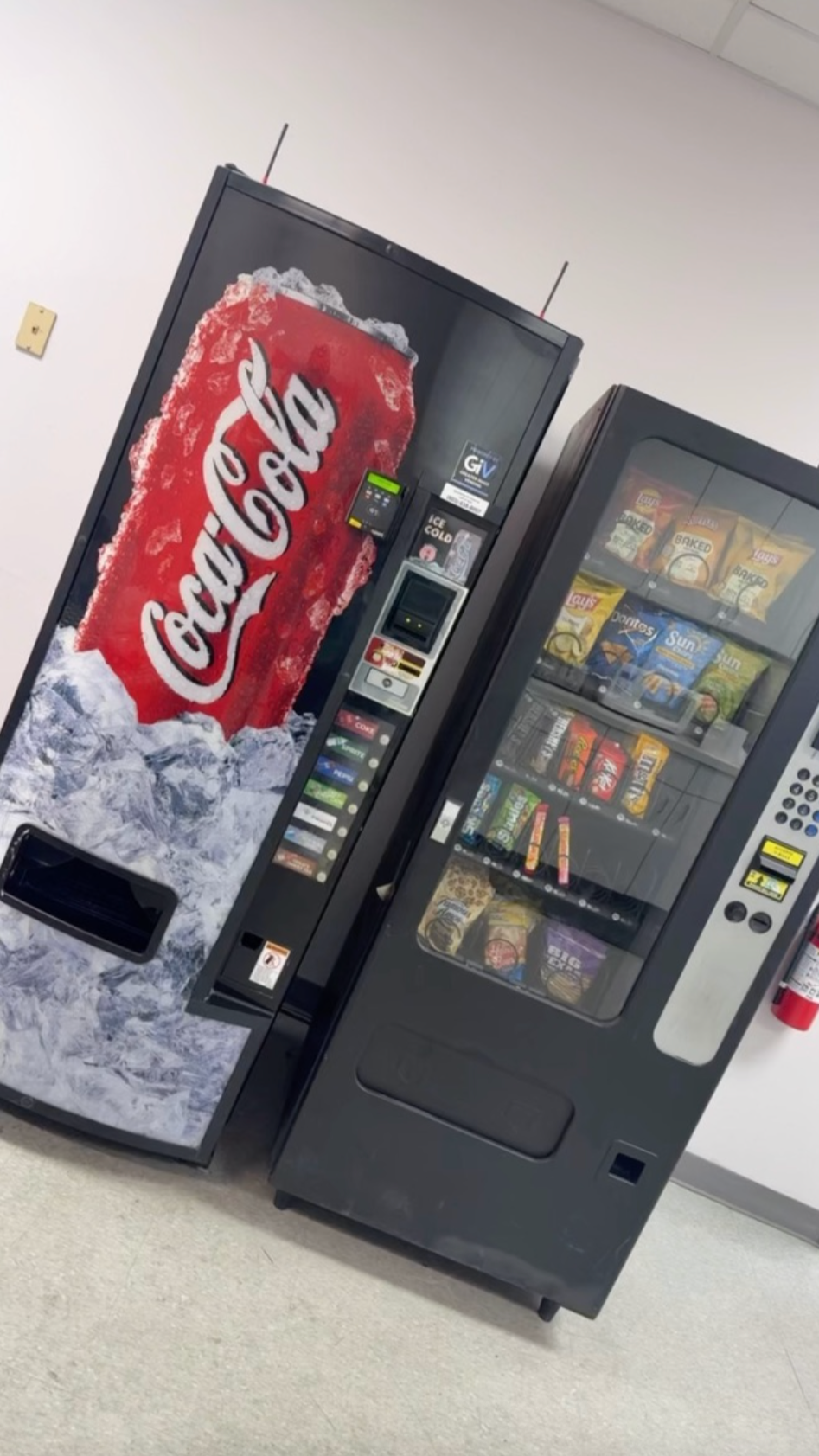 A vending machine with a Coca-Cola soda dispenser to the left and snack items, including chips and candy, inside a clear glass case on the right.