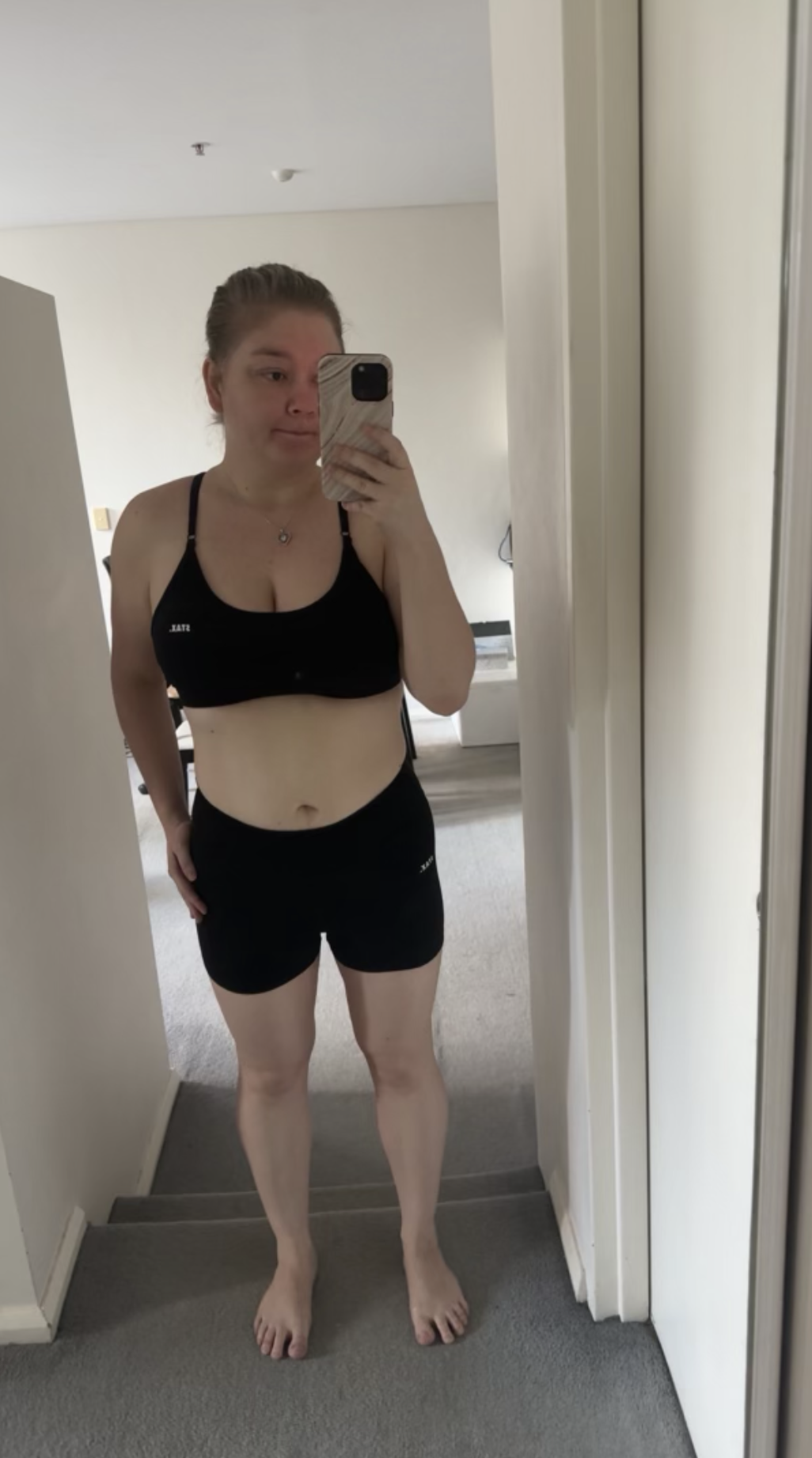 A woman in black sportswear taking a mirror selfie in a home interior.