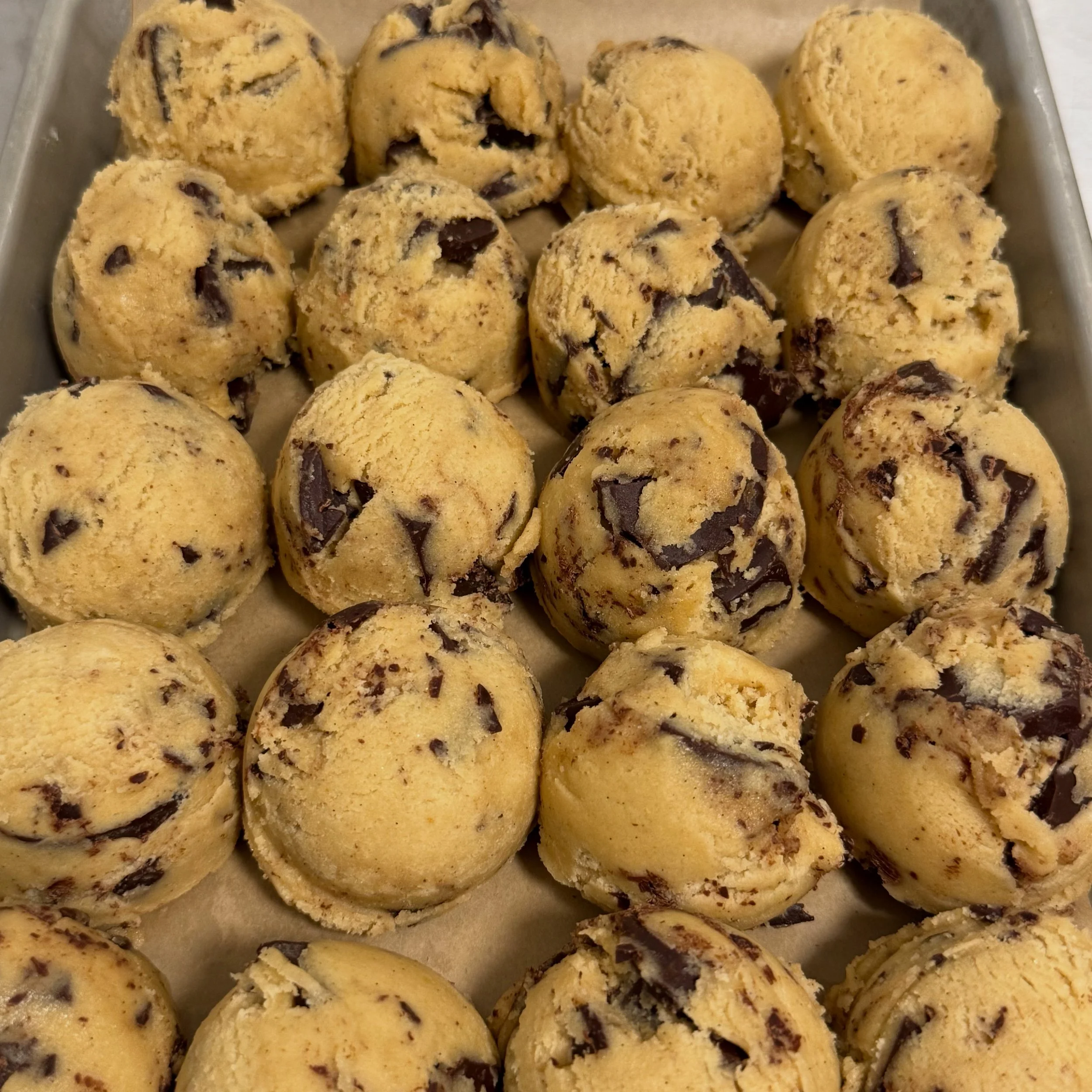 Bite-sized cookie dough balls with chocolate chips on a baking sheet.