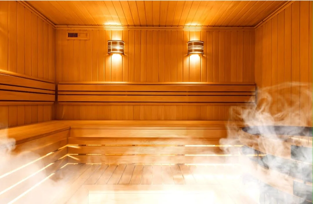 Interior of a traditional wooden sauna with steam rising and warm lighting.