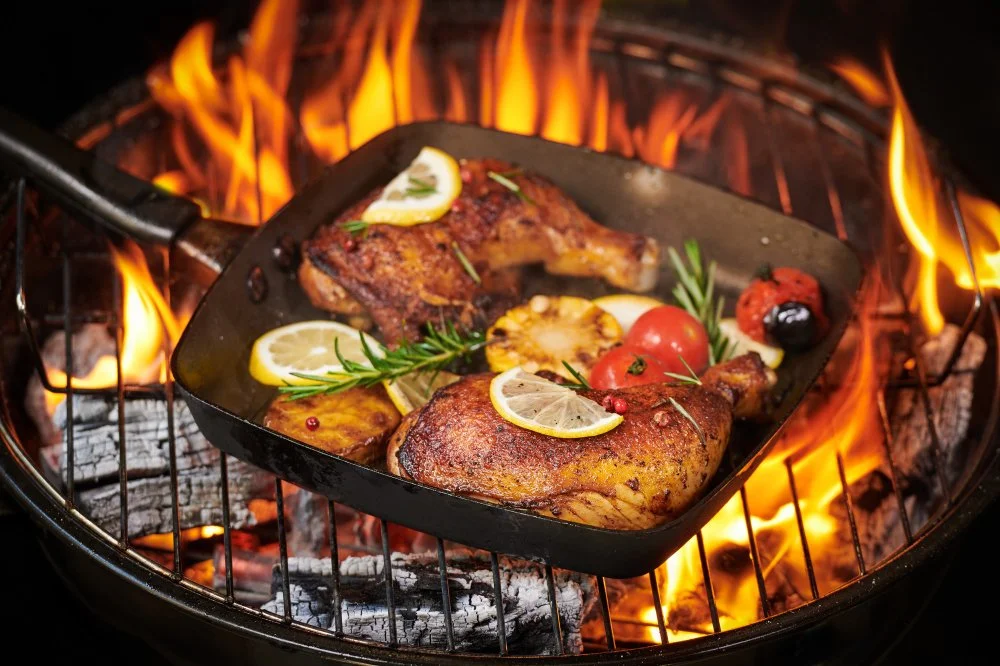 Meat with lemon slices, cherry tomatoes, rosemary, and cherry topping cooking on a grill over an open flame.