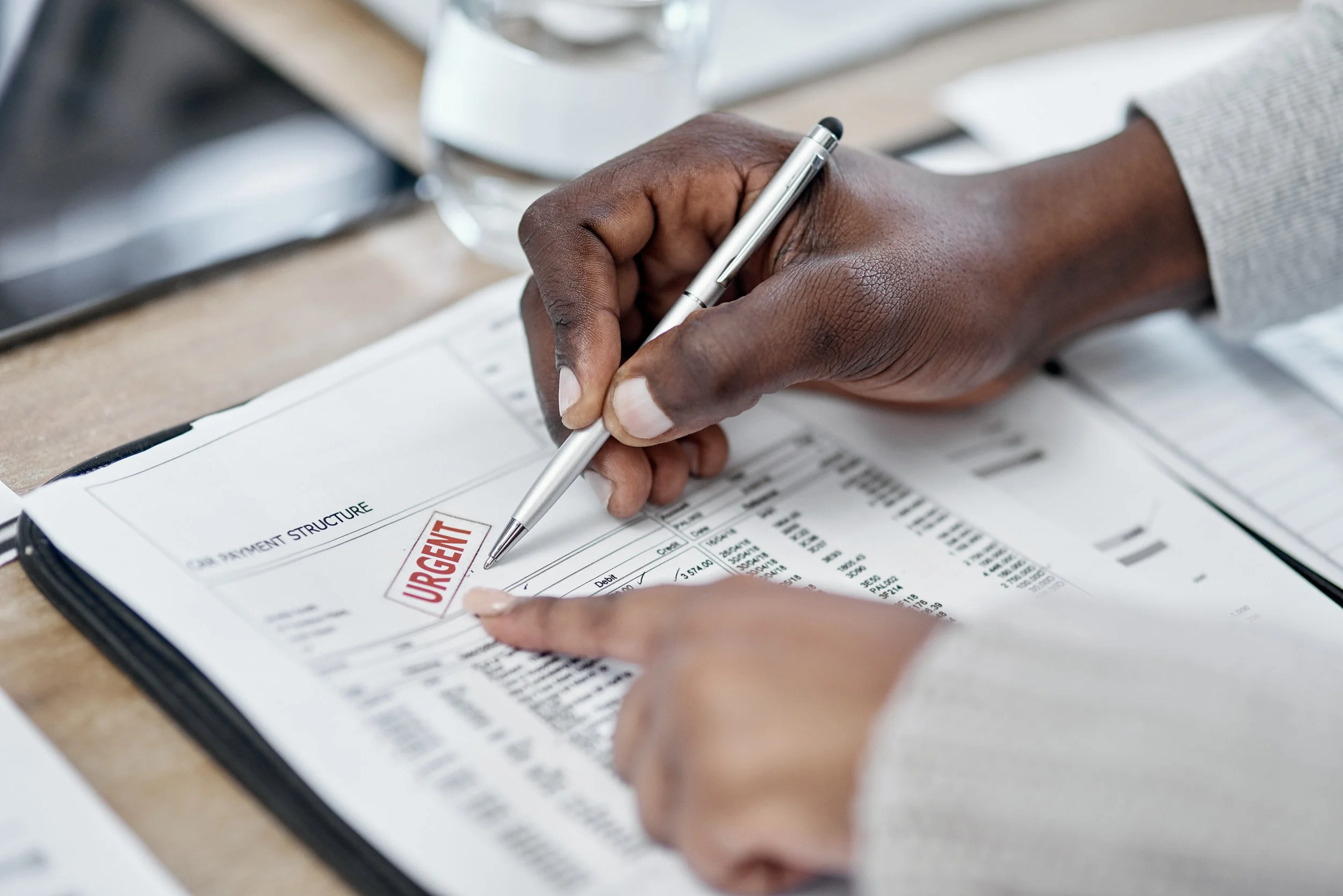 Close-up of a person pointing at an urgent payment structure document with a pen, on a desk.