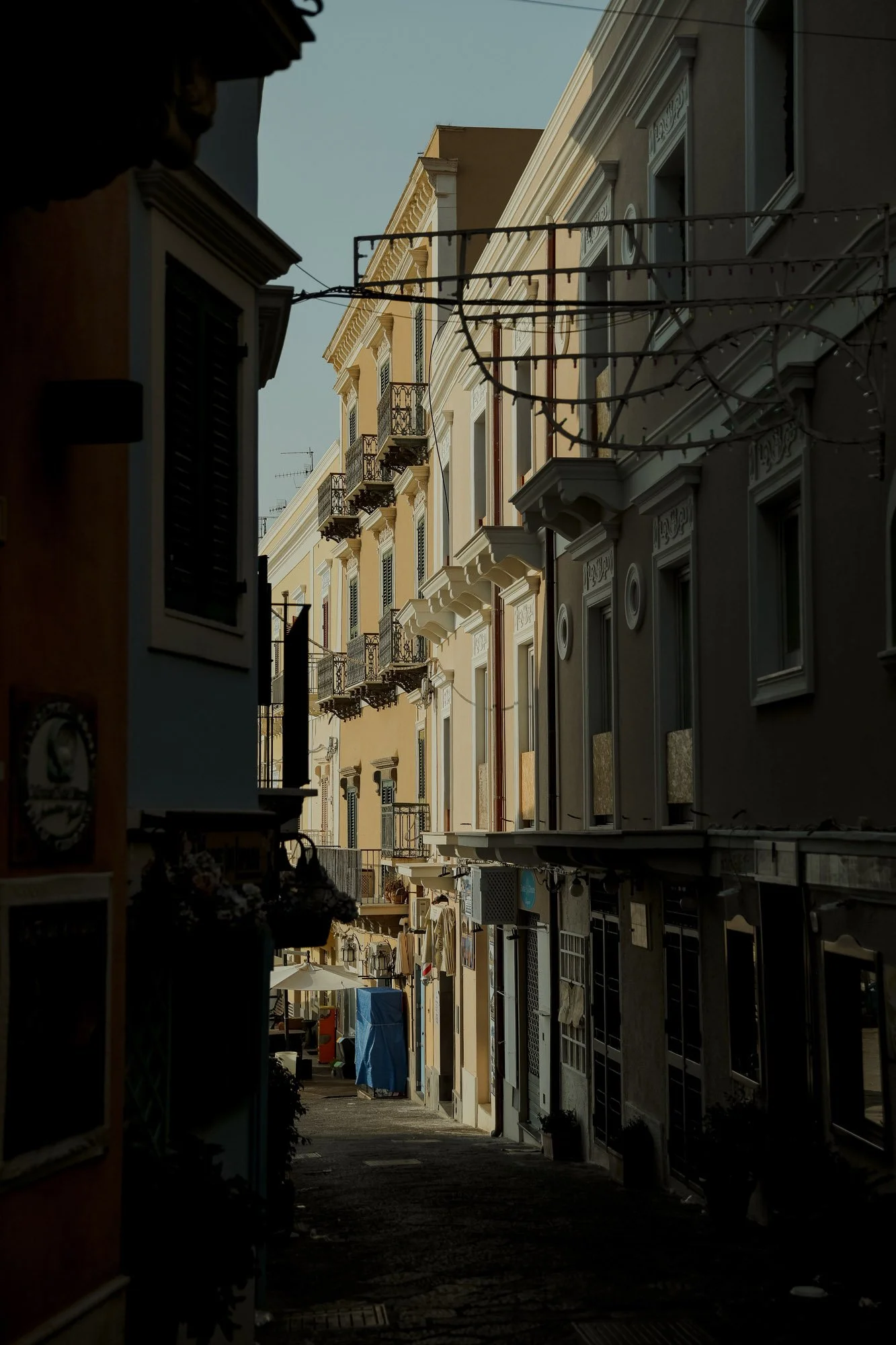 Narrow street with multi-story European-style buildings, balconies, and hanging string lights.