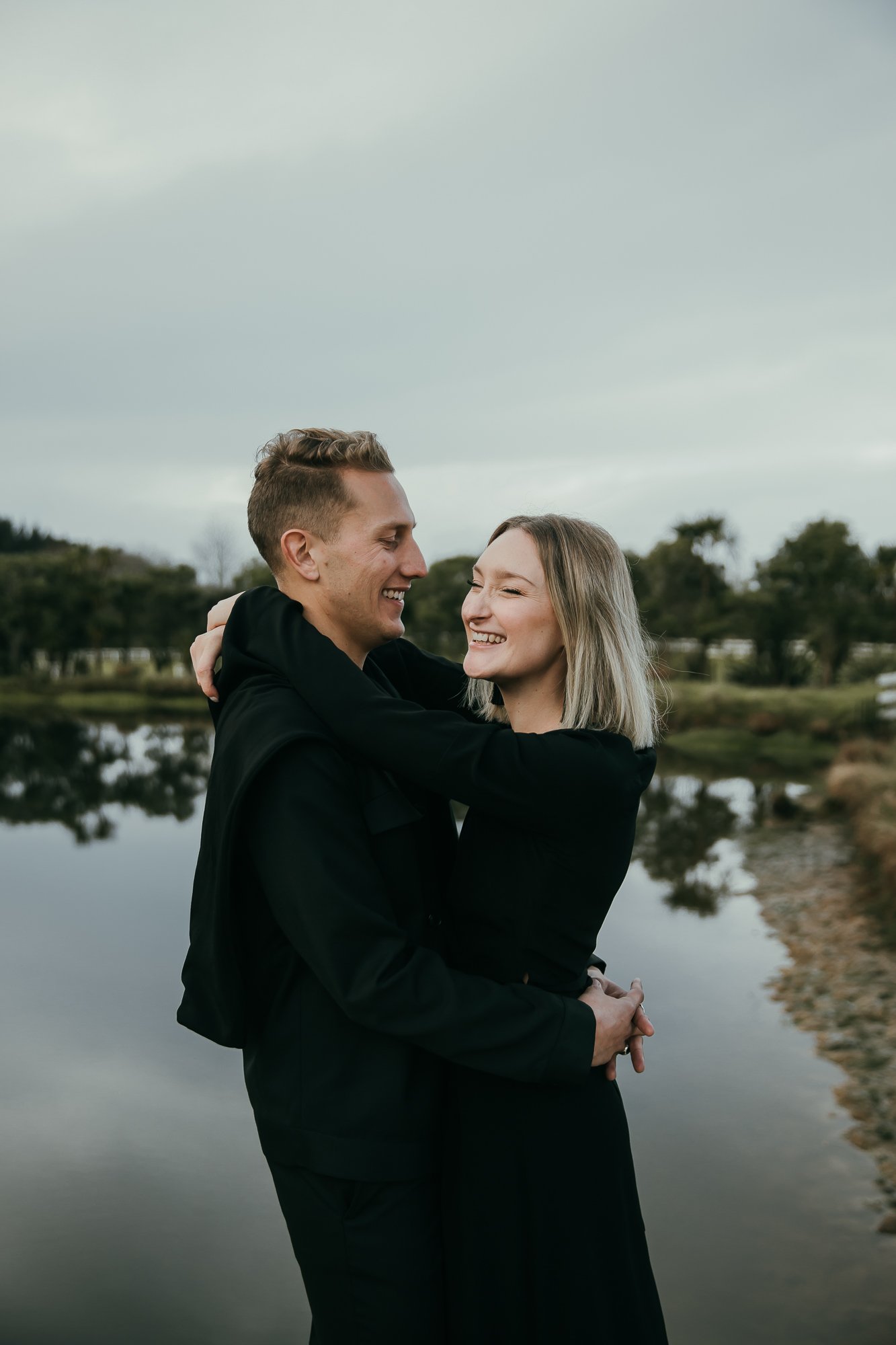 Bride and groom wearing all black standing laughing on a dock
