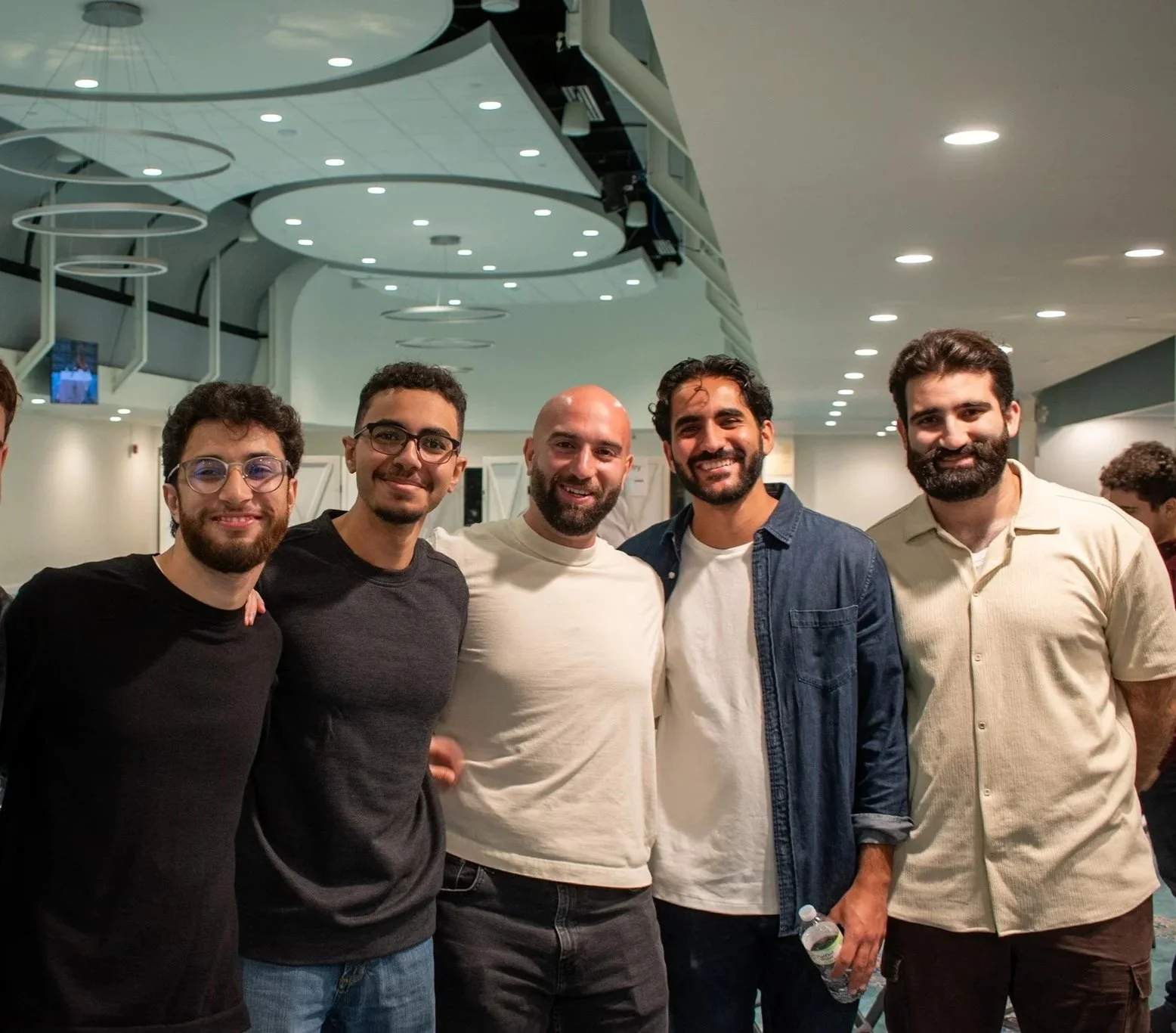 A group of five men standing close together indoors, smiling at the camera.