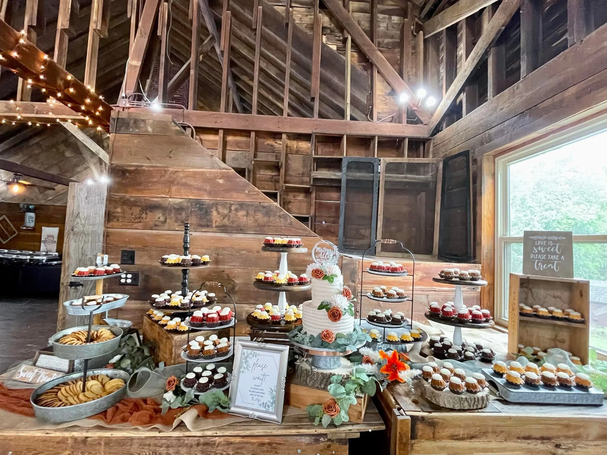 Dessert table rental with cupcakes, cookies, and a decorated cake in a rustic barn setting with string lights and a window. Dream Day Event Rentals, Vintage and Modern Decor and Floral Rentals, Freeport Illnois. Rent cake stands and serving ware.
