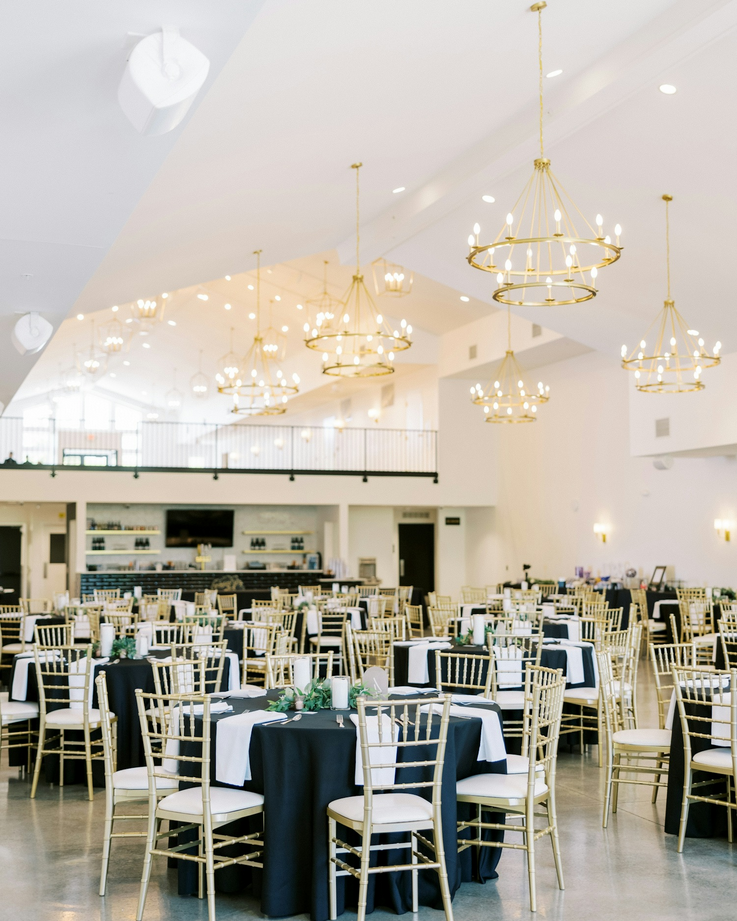 Elegant event space with round tables draped in black and white tablecloths, gold chiavari chairs, and gold chandeliers hanging from the ceiling. Dream Day Event Rentals, Vintage and Modern Decor and Floral Rentals, Freeport Illnois.