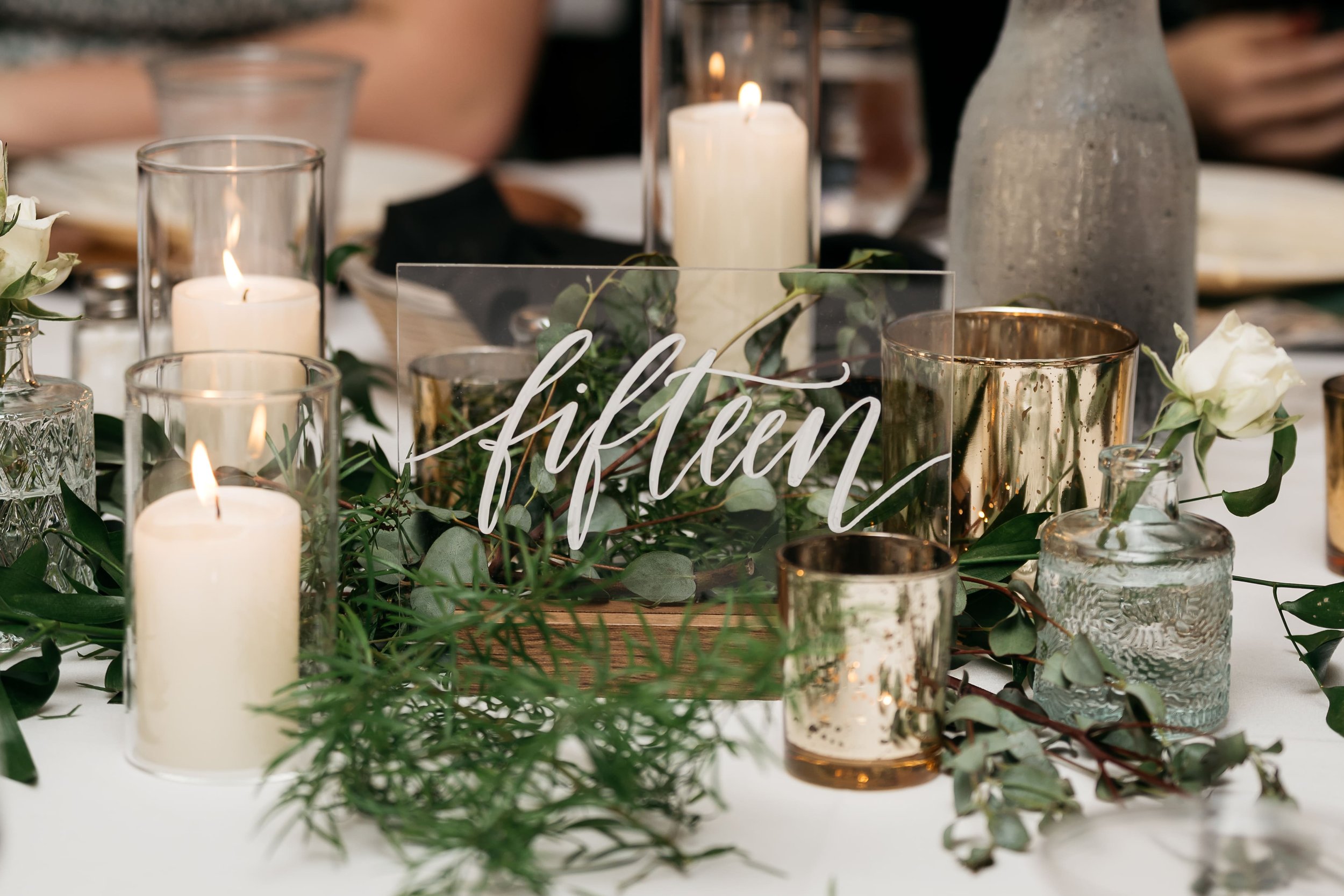Wedding table decoration with candles, greenery, and a wooden table number sign reading 'fifteen'. Dream Day Event Rentals, Vintage and Modern Decor and Floral Rentals, Freeport Illinois and Southern Wisconsin.