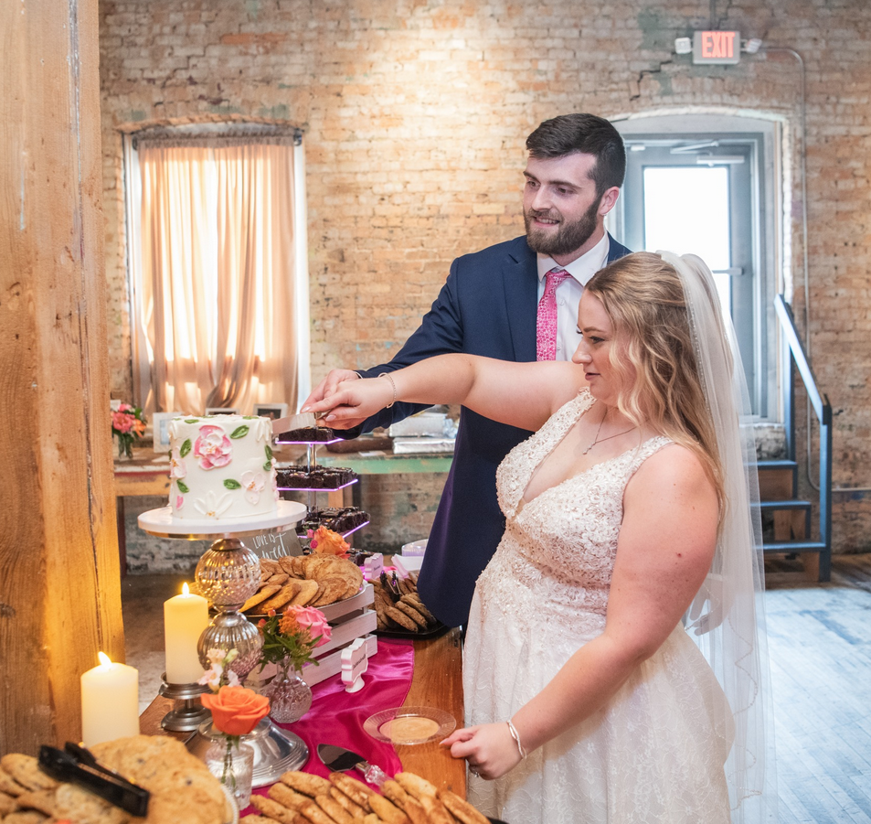 Bride and groom cutting the wedding cake together at a reception, with cookies and candles on the table. Dream Day Event Rentals, Vintage and Modern Decor and Floral Rentals, Freeport Illnois.