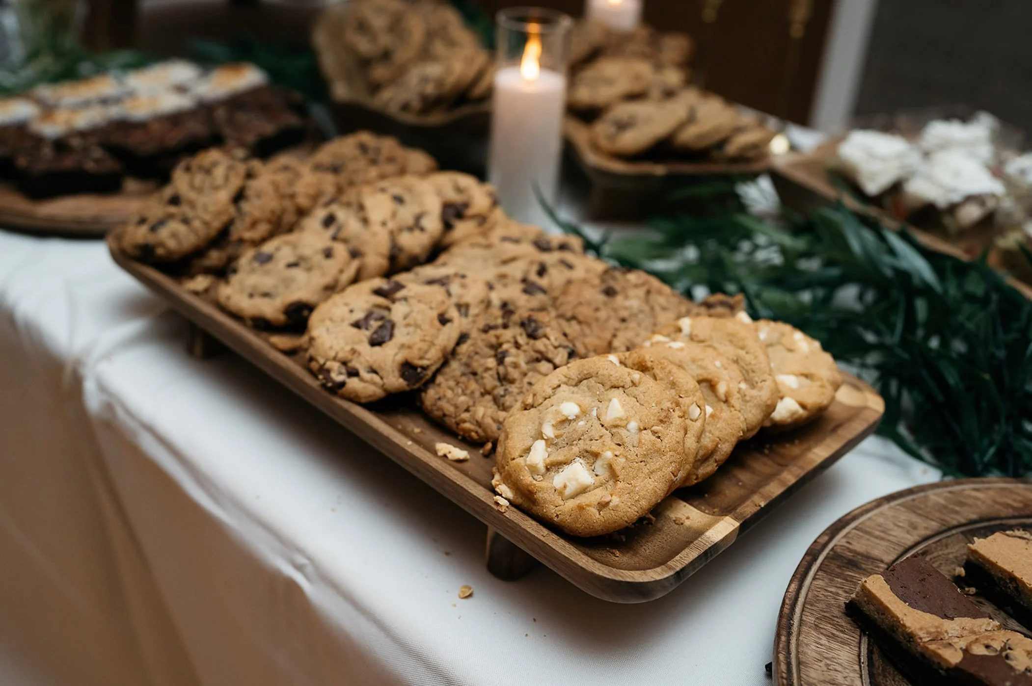 Assorted cookies on a wooden tray, decorated with a lit candle and greenery, on a white tablecloth. Dream Day Event Rentals, Vintage and Modern Decor and Floral Rentals, Freeport Illnois.