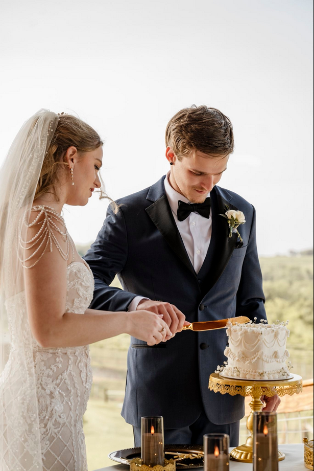 Bride and groom cutting a wedding cake outdoors with a scenic landscape in the background. Dream Day Event Rentals, Vintage and Modern Decor and Floral Rentals, Freeport Illnois.