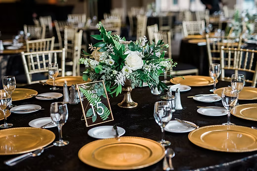 Wedding reception table with gold chargers, white plates, silverware, glasses, and a floral centerpiece. Dream Day Event Rentals, Vintage and Modern Decor and Floral Rentals, Freeport Il