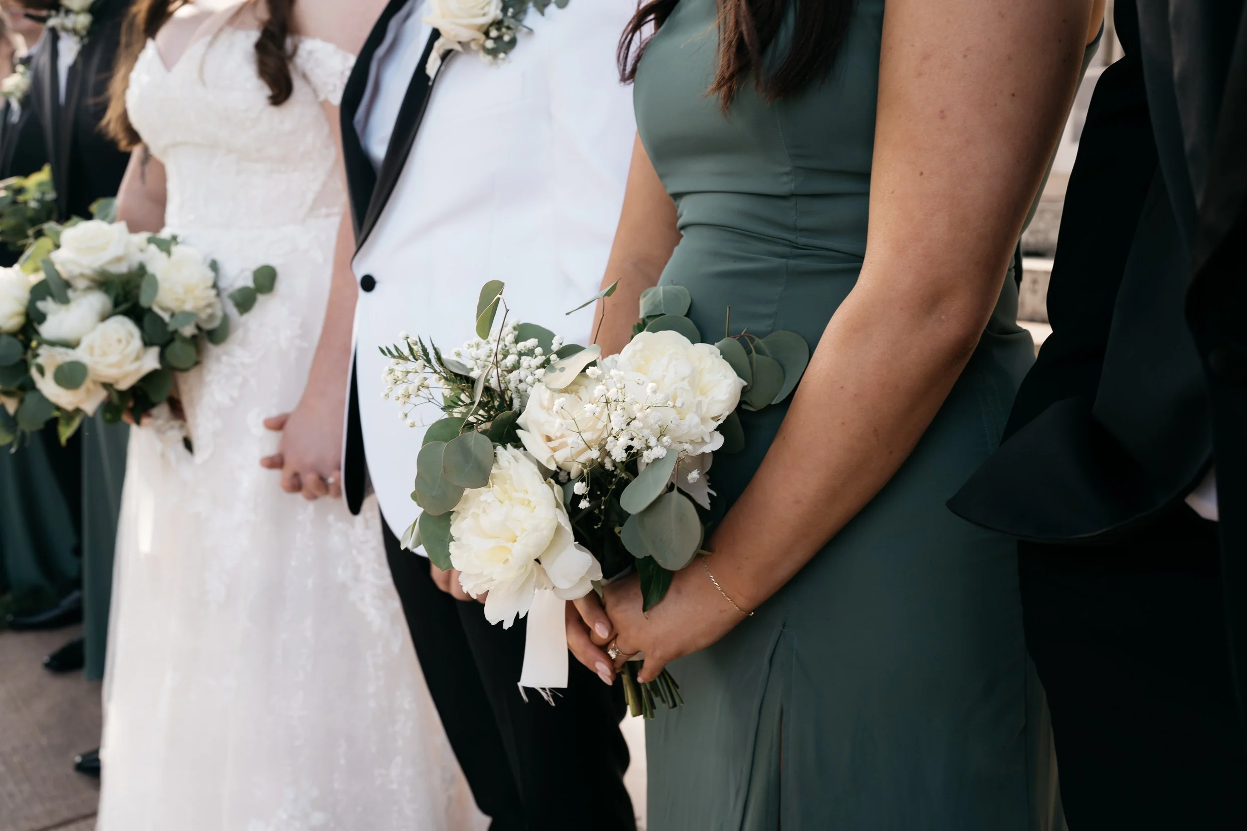 Close-up of women holding bridal bouquets at a wedding, with brides in white dress and women in green dresses, along with men in black suits. Dream Day Event Rentals, Vintage and Modern Decor and Floral Rentals, Freeport Illnois.