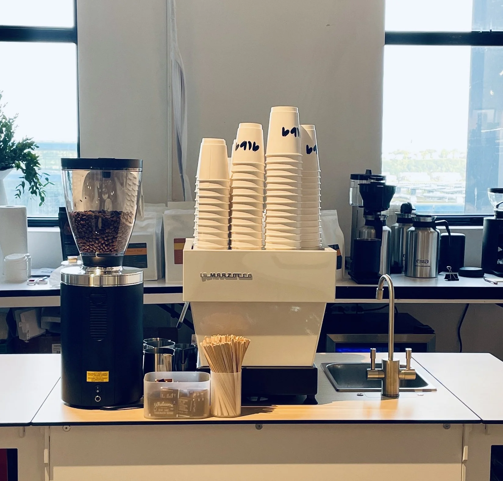 Coffee station with stacked cups, coffee beans in a grinder, and various coffee-making equipment.