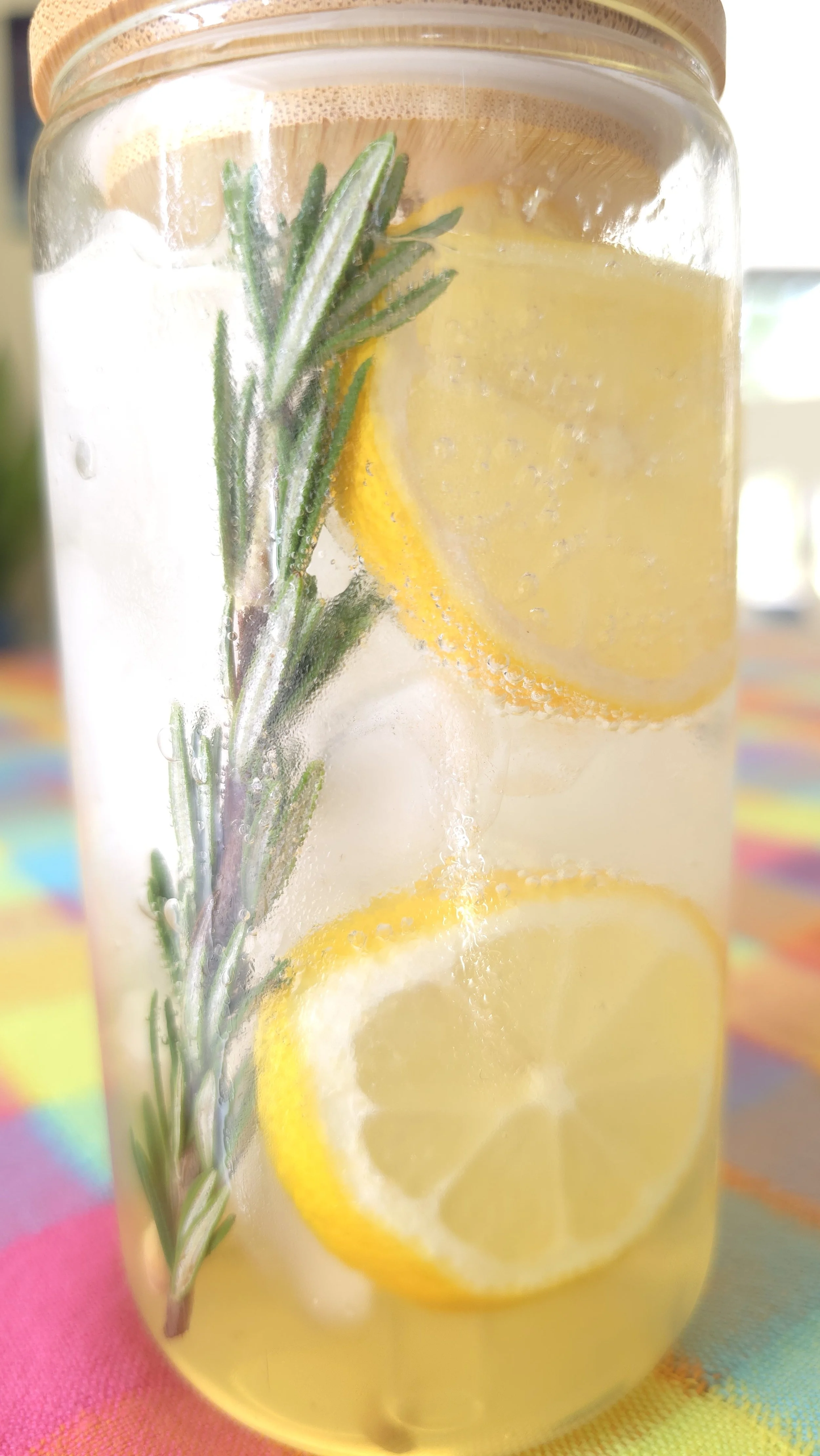 A glass jar filled with soda water, lemon slices, and fresh rosemary sprigs.